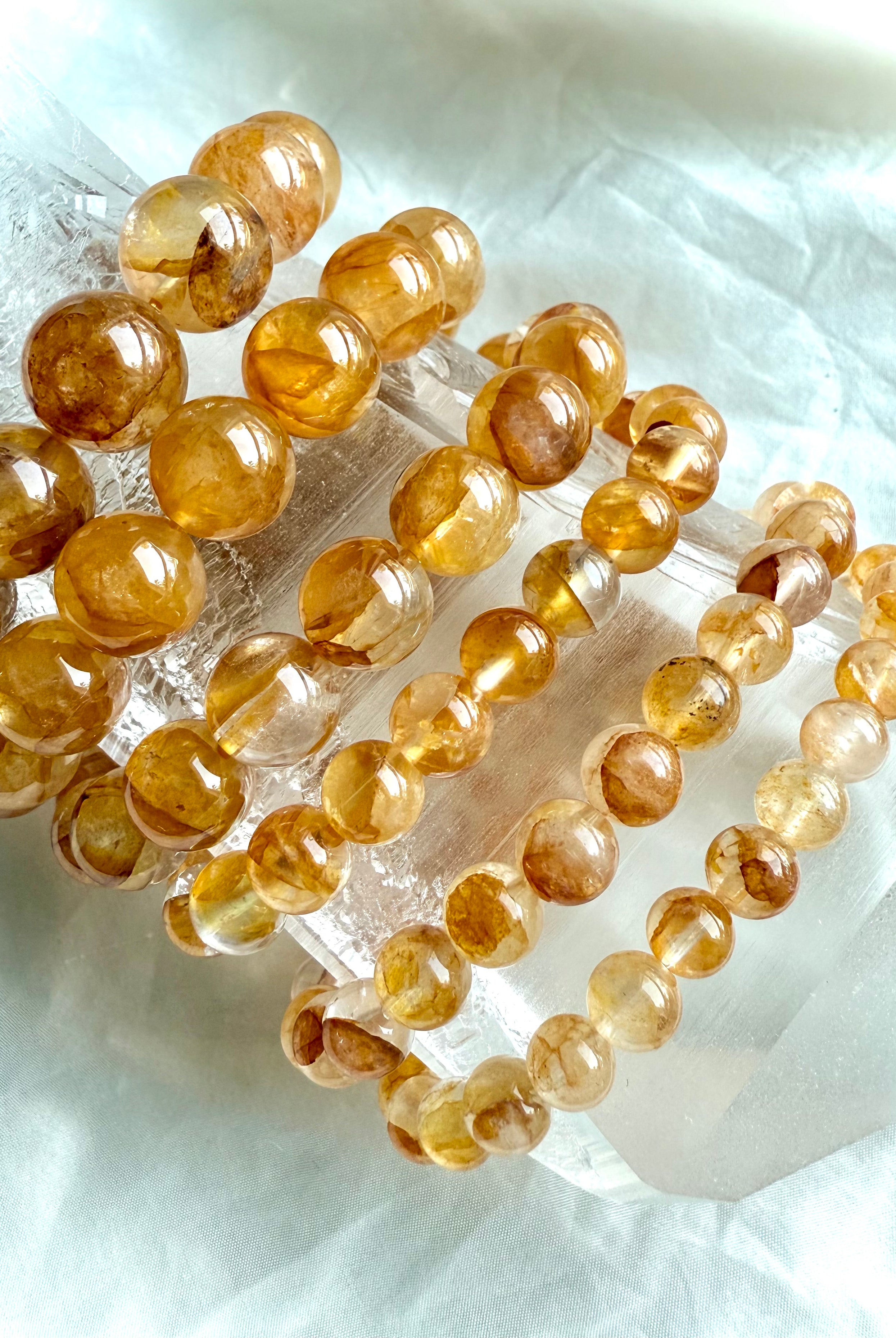 Golden Healer Quartz beaded bracelet stack on quartz point, highlighting radiant golden tones, transparency, and natural variation in bead sizes.