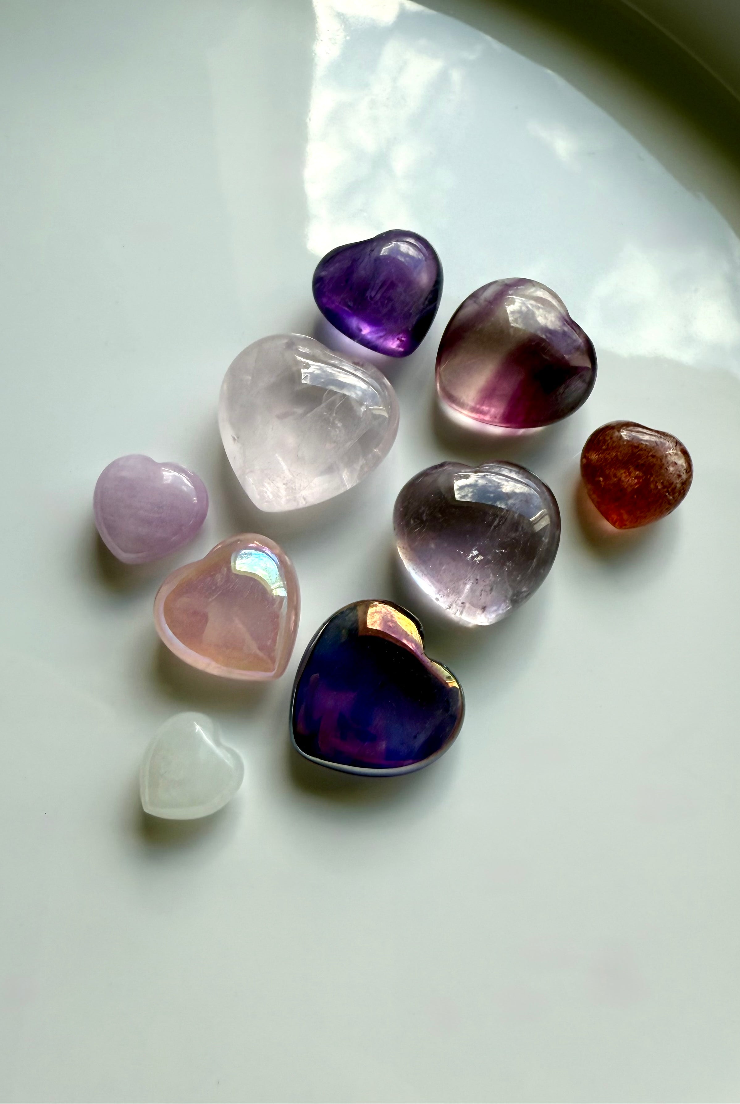 Wide view of pink and purple mini crystal hearts on white, highlighting color, aura coating, and polished finish.