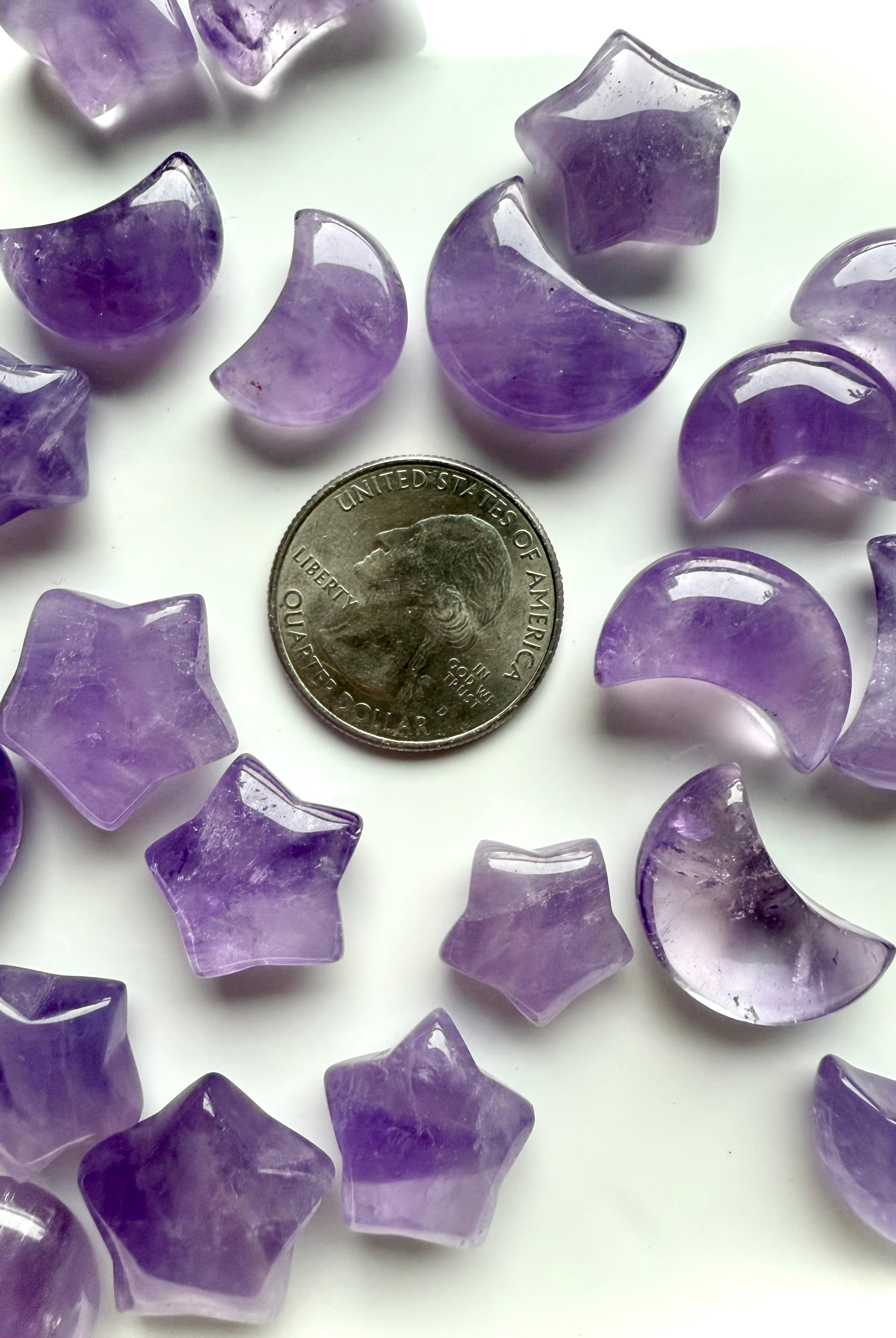 Close-up of amethyst star and crescent moon carvings shown with a US quarter for scale, highlighting smooth polish and translucence