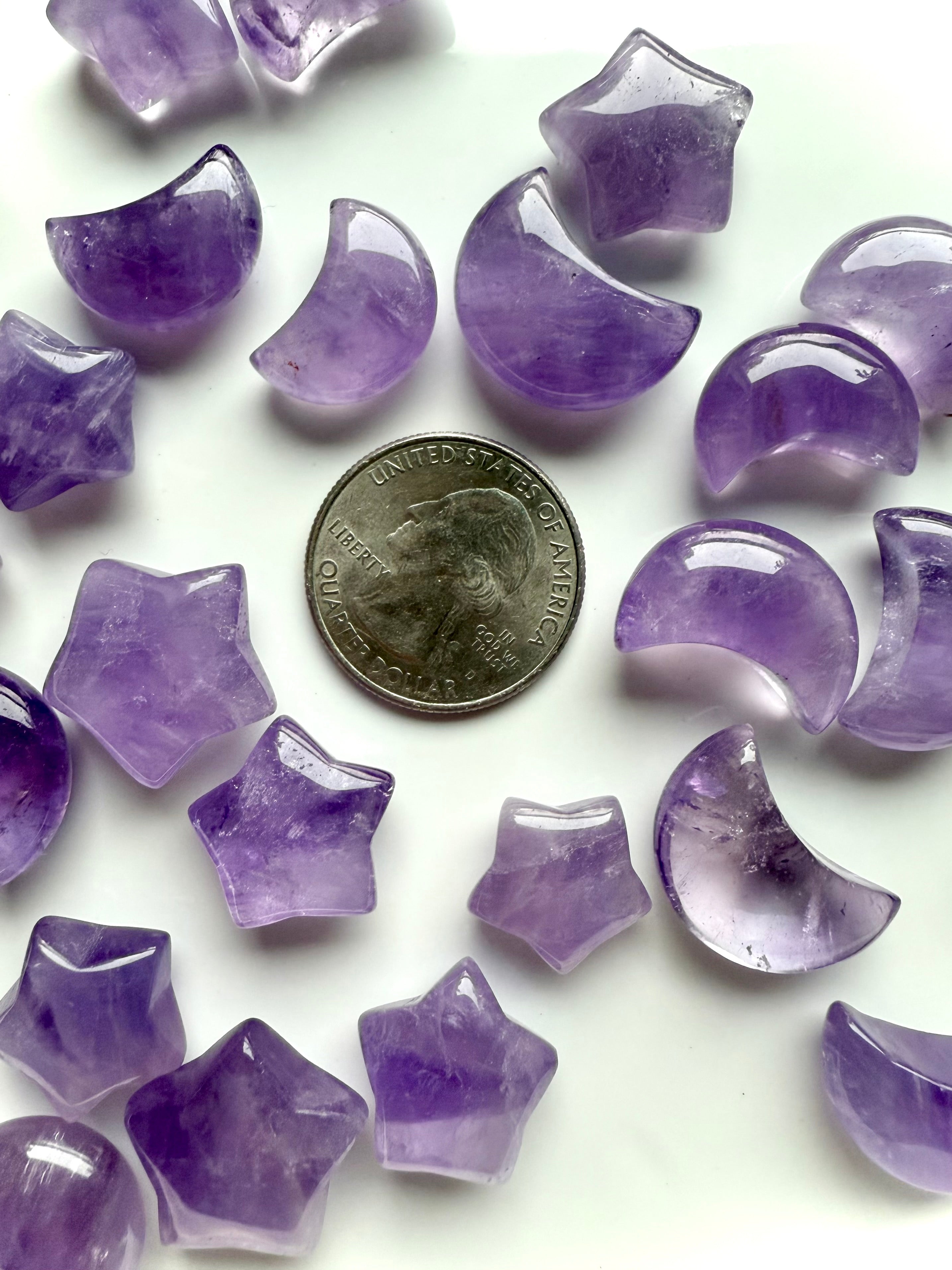 Close-up of amethyst star and crescent moon carvings shown with a US quarter for scale, highlighting smooth polish and translucence