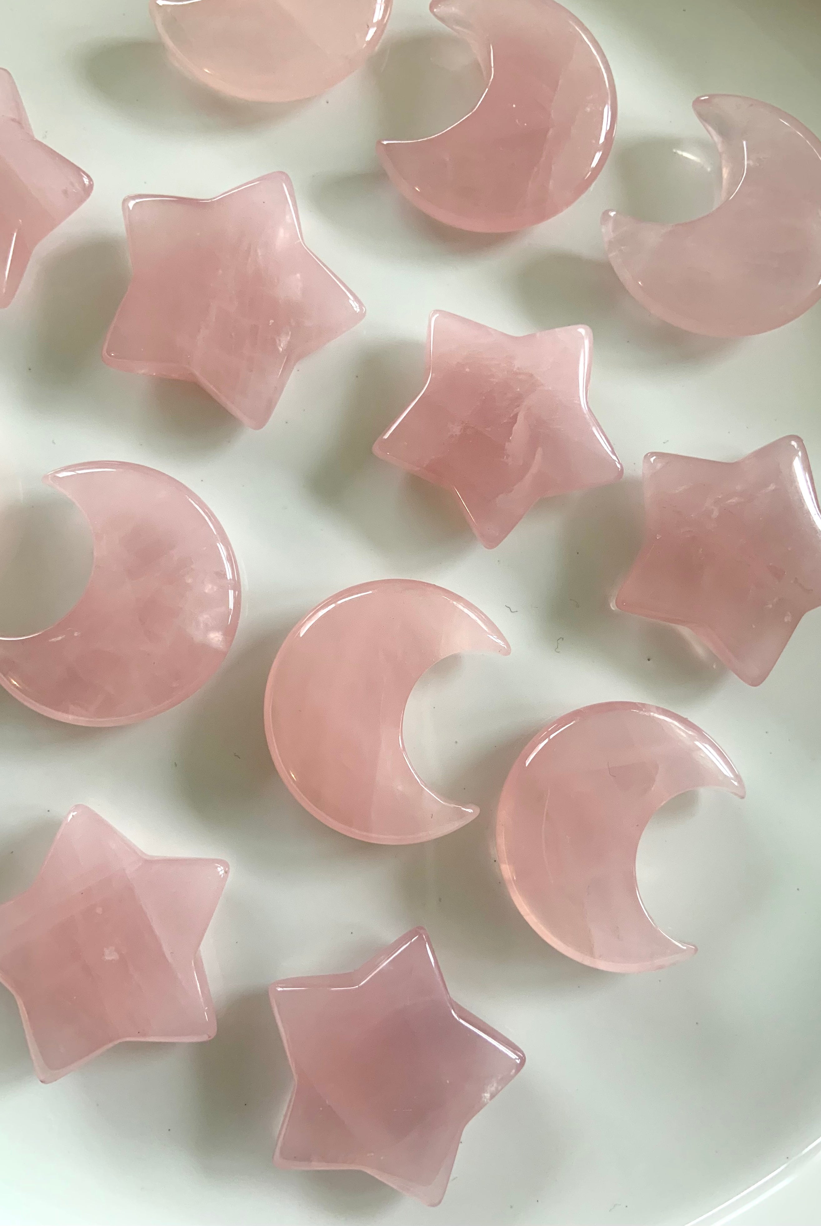 Rows of rose quartz moons and stars on white. Madagascar rose quartz carvings for unconditional love, heart healing & emotional balance.