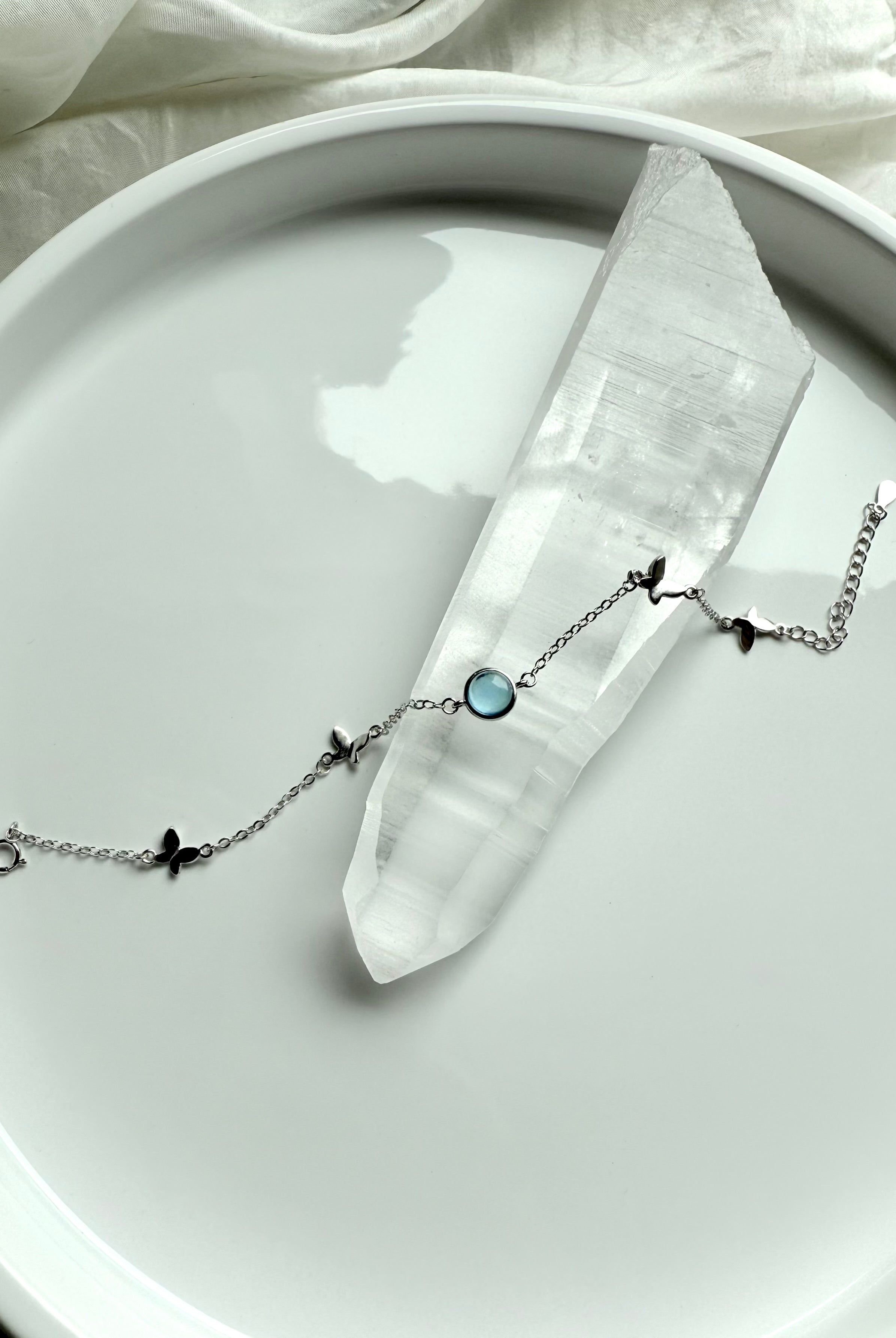 Aquamarine gemstone bracelet with silver butterfly charms displayed across a clear quartz point for spiritual healing and clarity