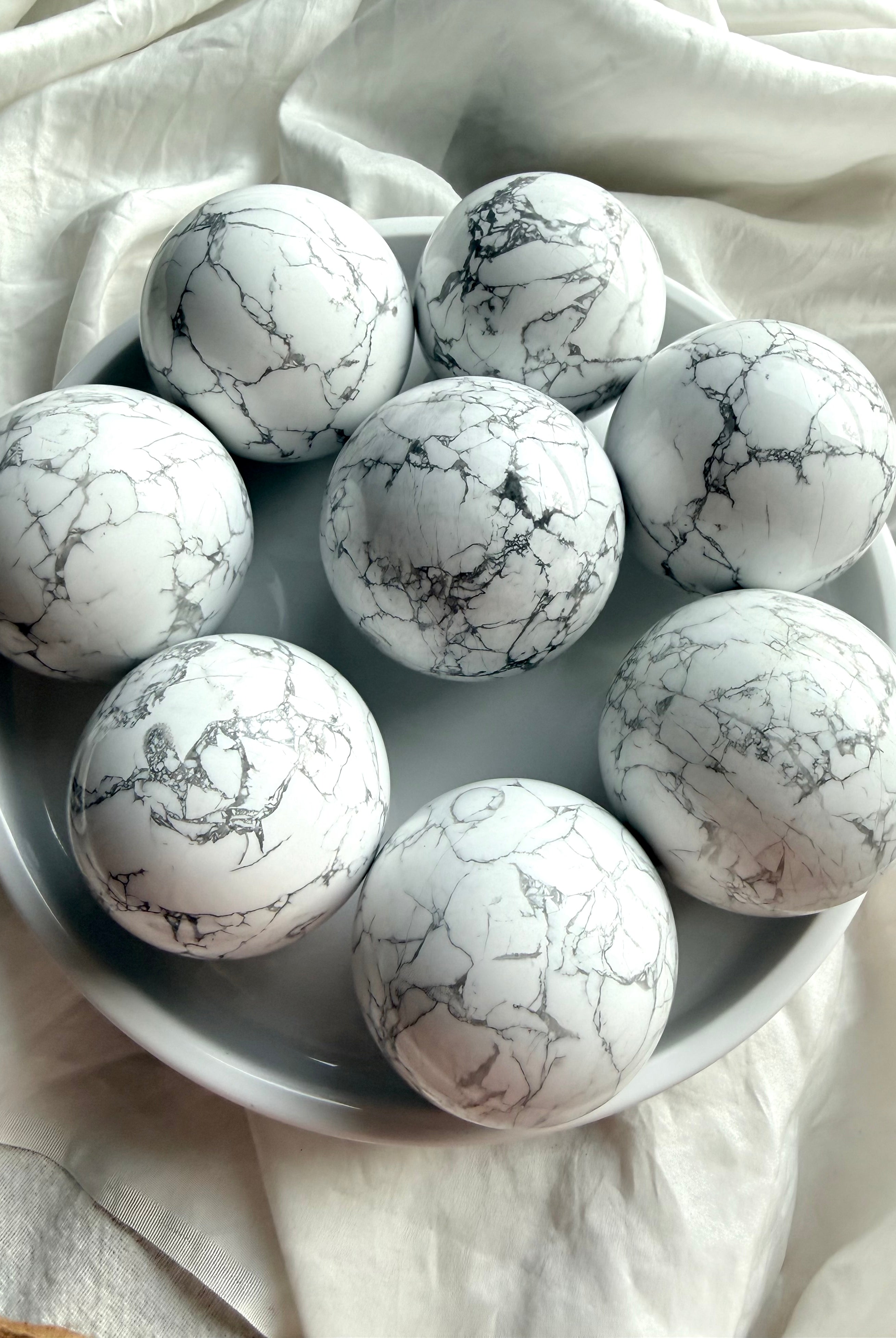 Assorted polished Howlite crystal spheres on white tray, natural white stone with gray veining for anxiety relief and serene altar décor