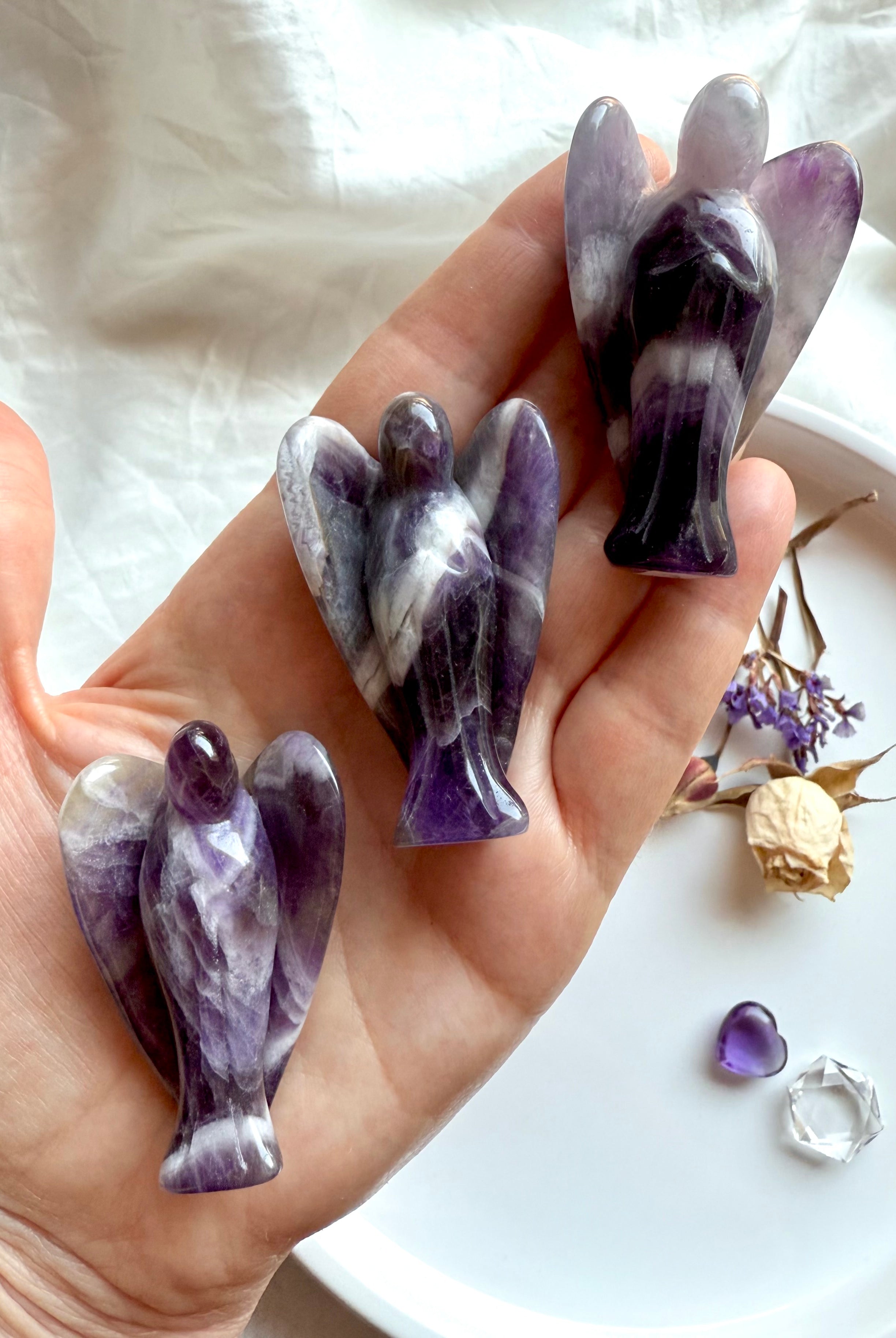 Hand holding three Dream Amethyst angel carvings with bold Chevron Amethyst patterns – crystal angels for Third Eye and Crown Chakra healing, spiritual support, and gifting