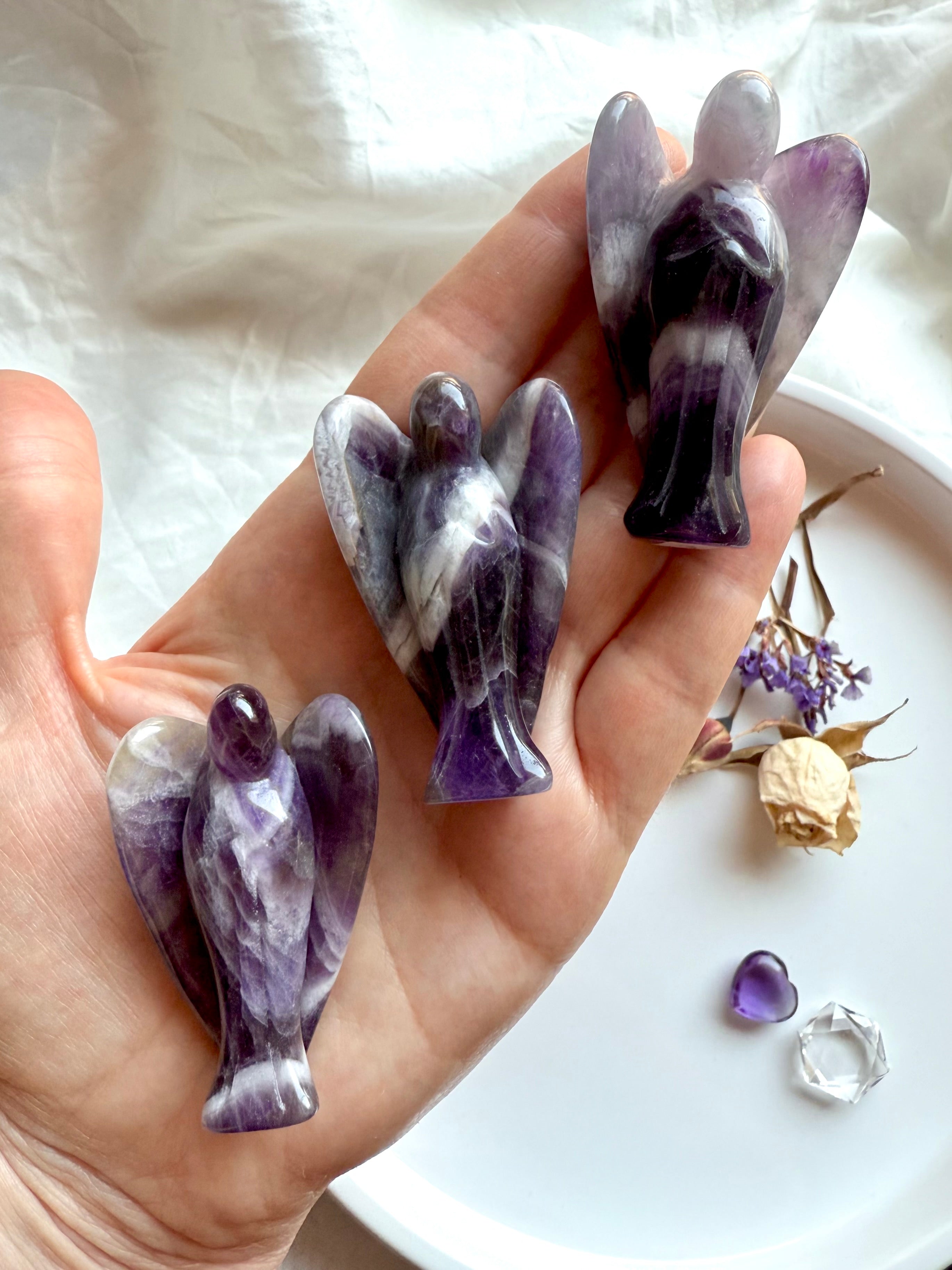 Hand holding three Dream Amethyst angel carvings with bold Chevron Amethyst patterns – crystal angels for Third Eye and Crown Chakra healing, spiritual support, and gifting