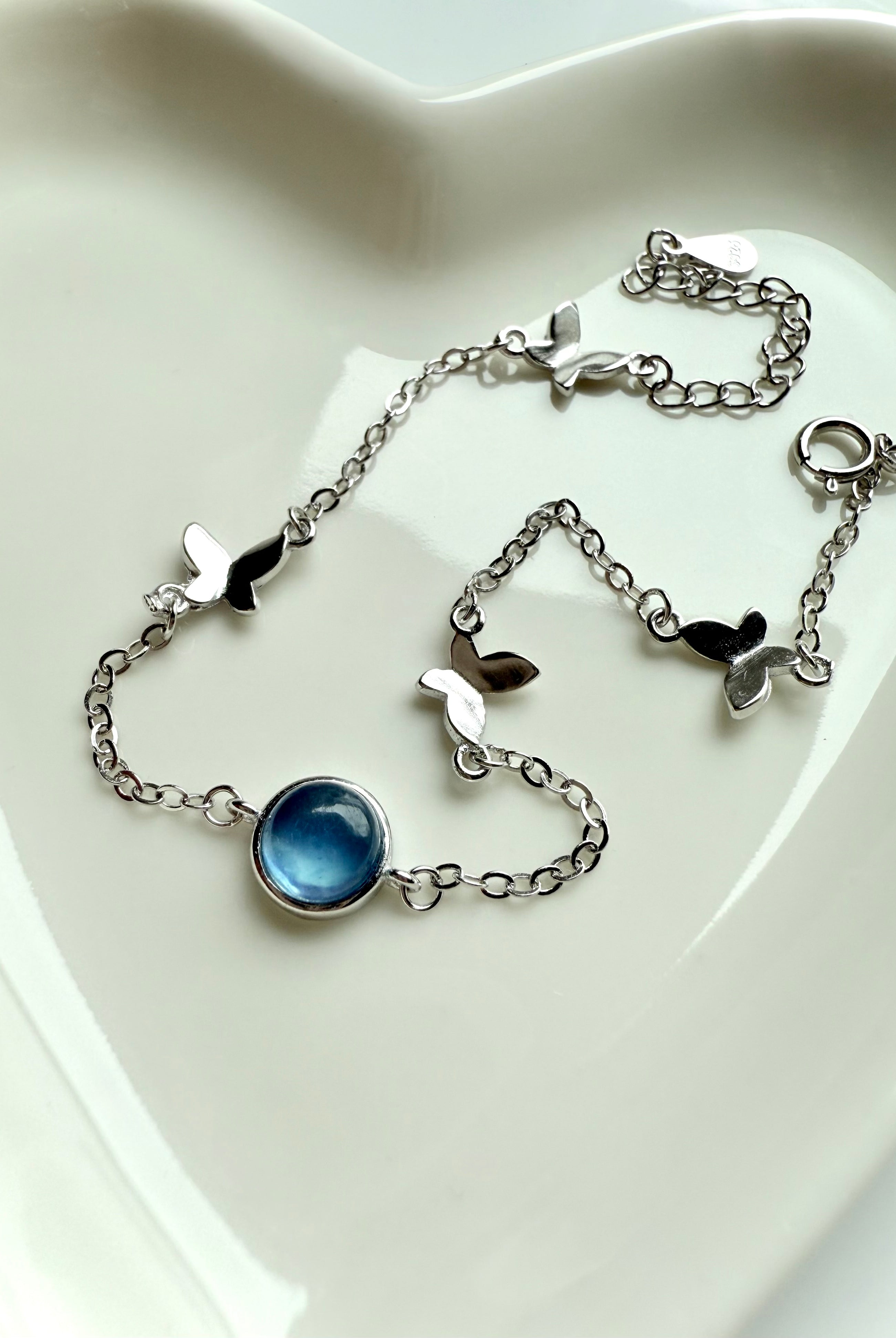 Aquamarine butterfly bracelet with dainty sterling silver chain styled in a heart-shaped dish — March birthstone jewelry for peace, clarity, and throat chakra healing