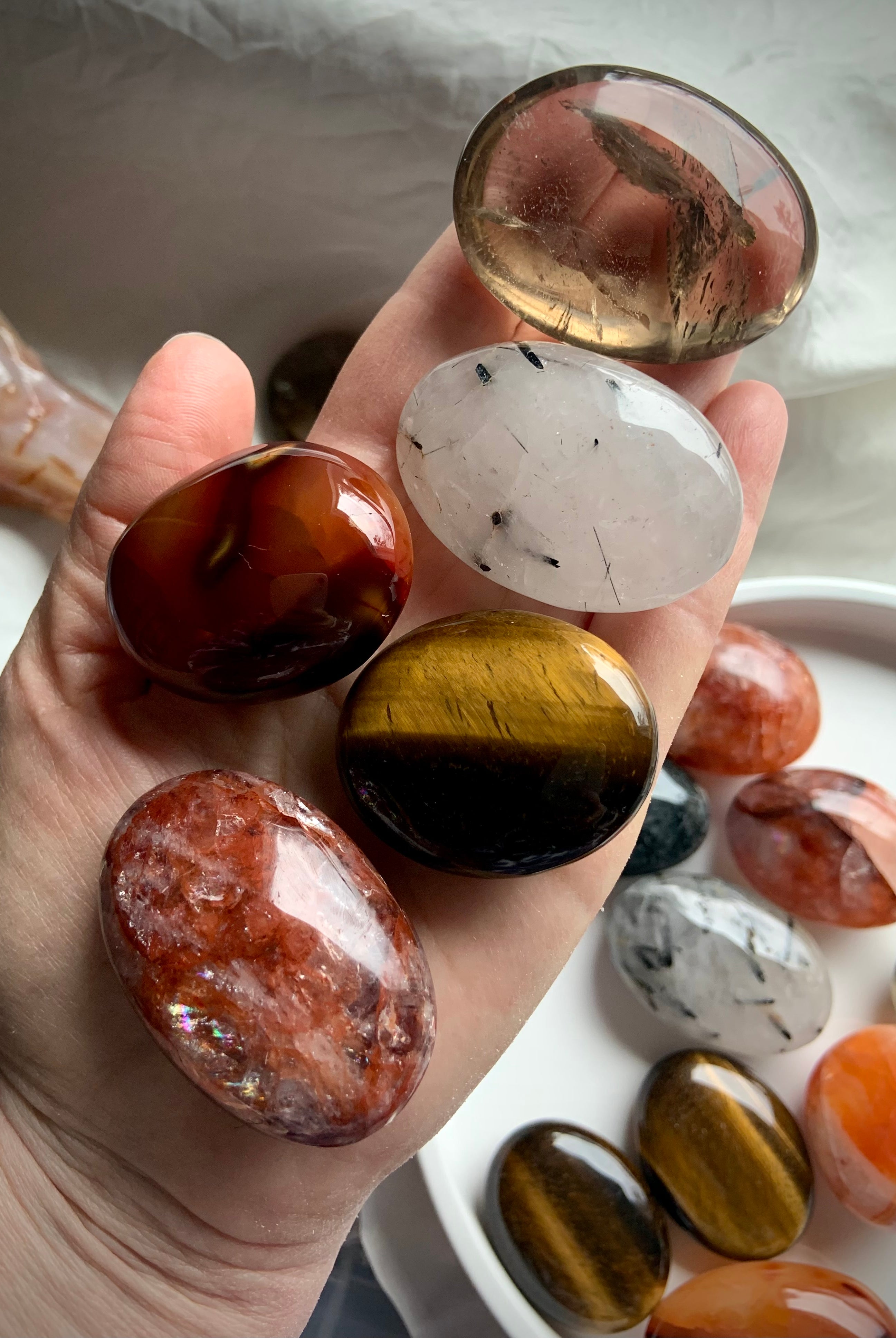 Chakra healing palm stones shown on hand with more stones in the background — polished crystals for grounding, motivation & confidence.