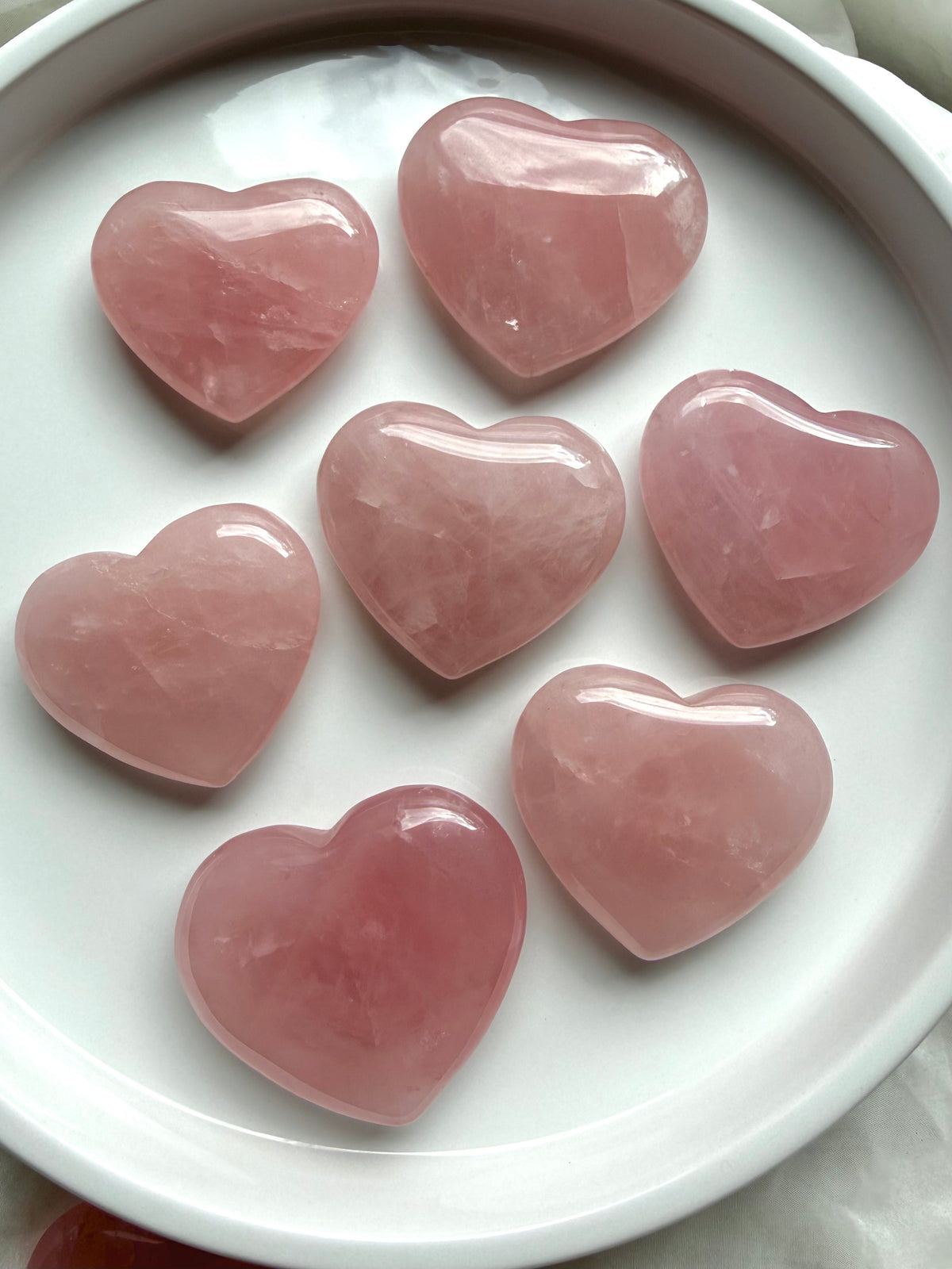 Rose Quartz heart crystals arranged on a white dish showing soft blush pink color and natural translucence