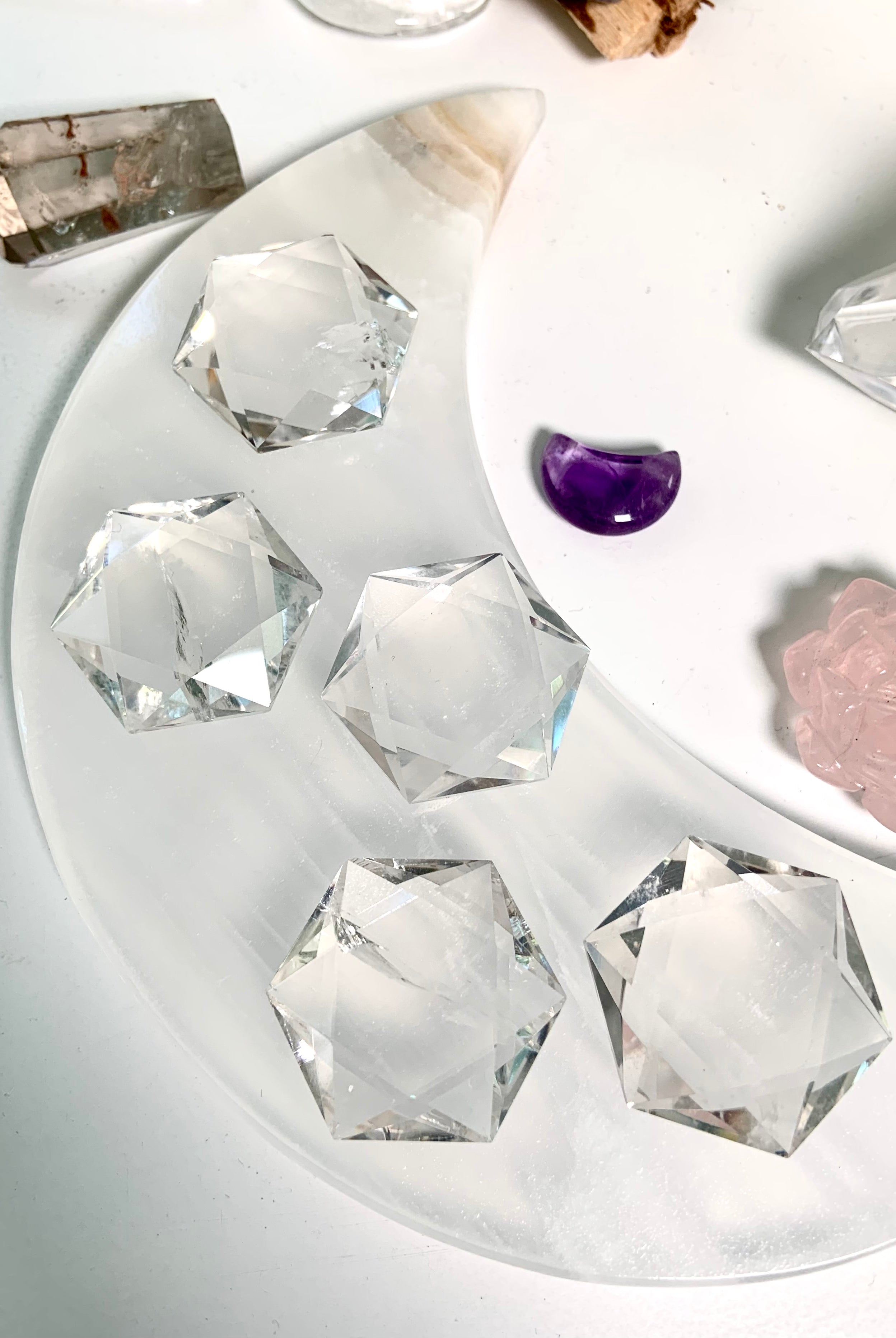 Overhead view of large Clear Quartz hexagons arranged on white moon plate with surrounding crystals
