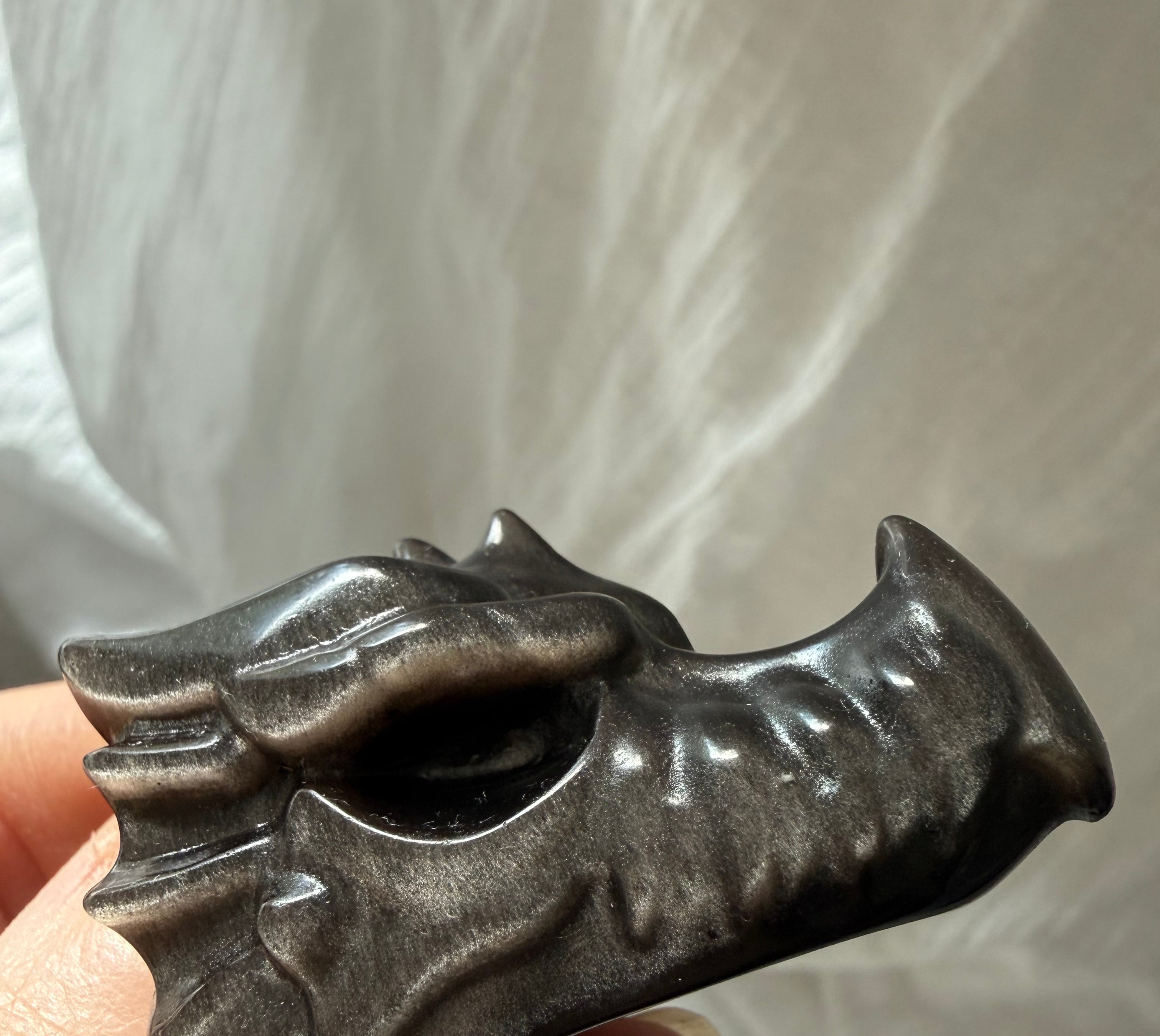 close-up of silver sheen obsidian dragon carving in hand highlighting polished surface and natural flash, stone for deep healing and protection