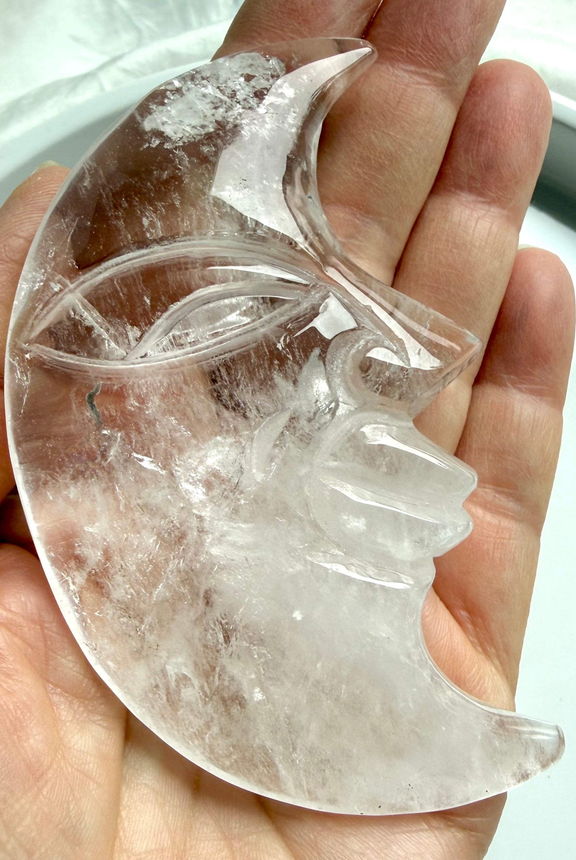 Clear Quartz Moon Face carving resting in hand, showcasing detailed carving on both sides and water-clear crystal clarity