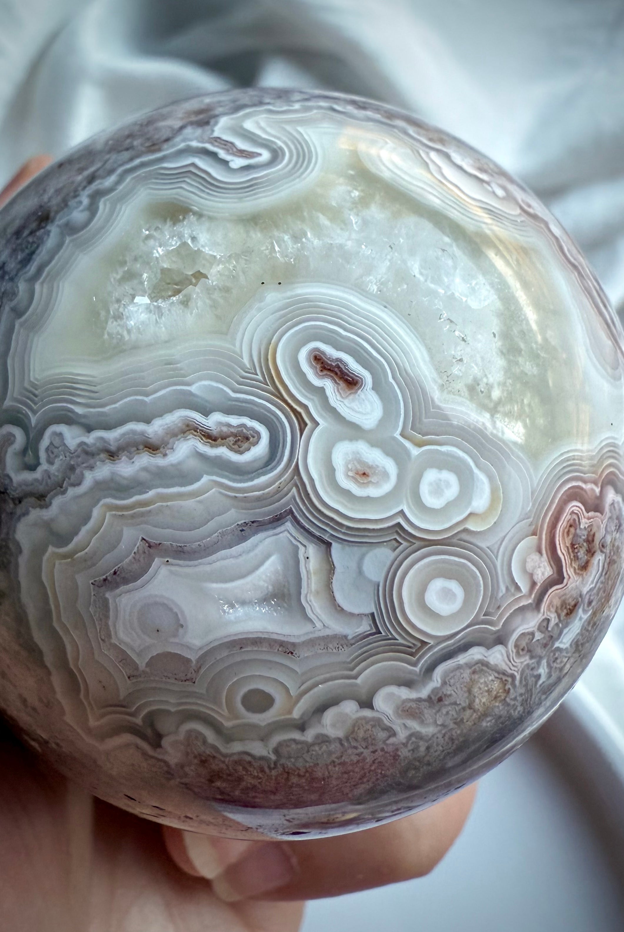 Close-up of Crazy Lace Agate sphere with creamy white banding, orbicular patterns, and exposed quartz window