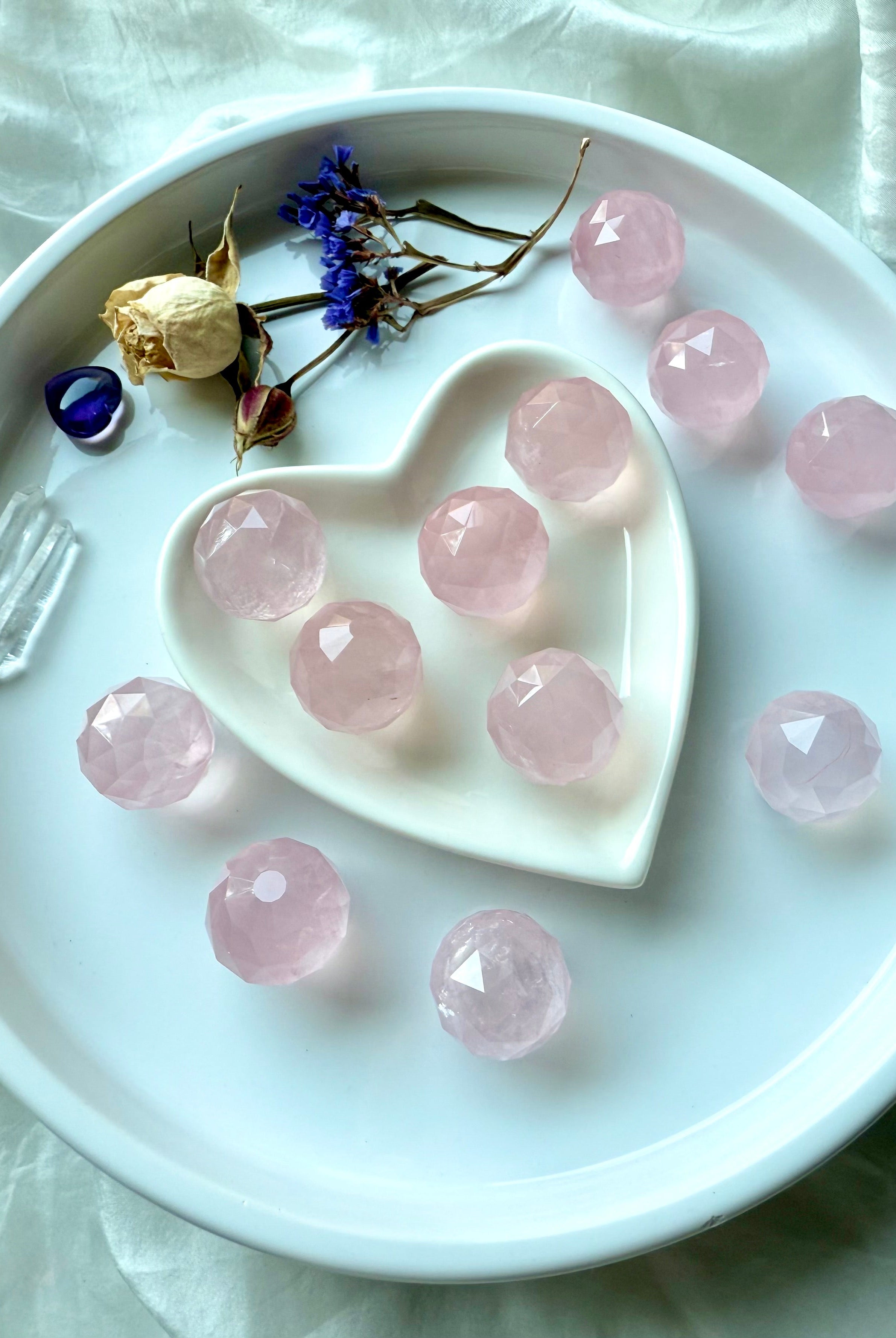 Faceted rose quartz mini spheres in a white heart-shaped dish with dried flowers and crystals. Soothing pink crystals for peace.