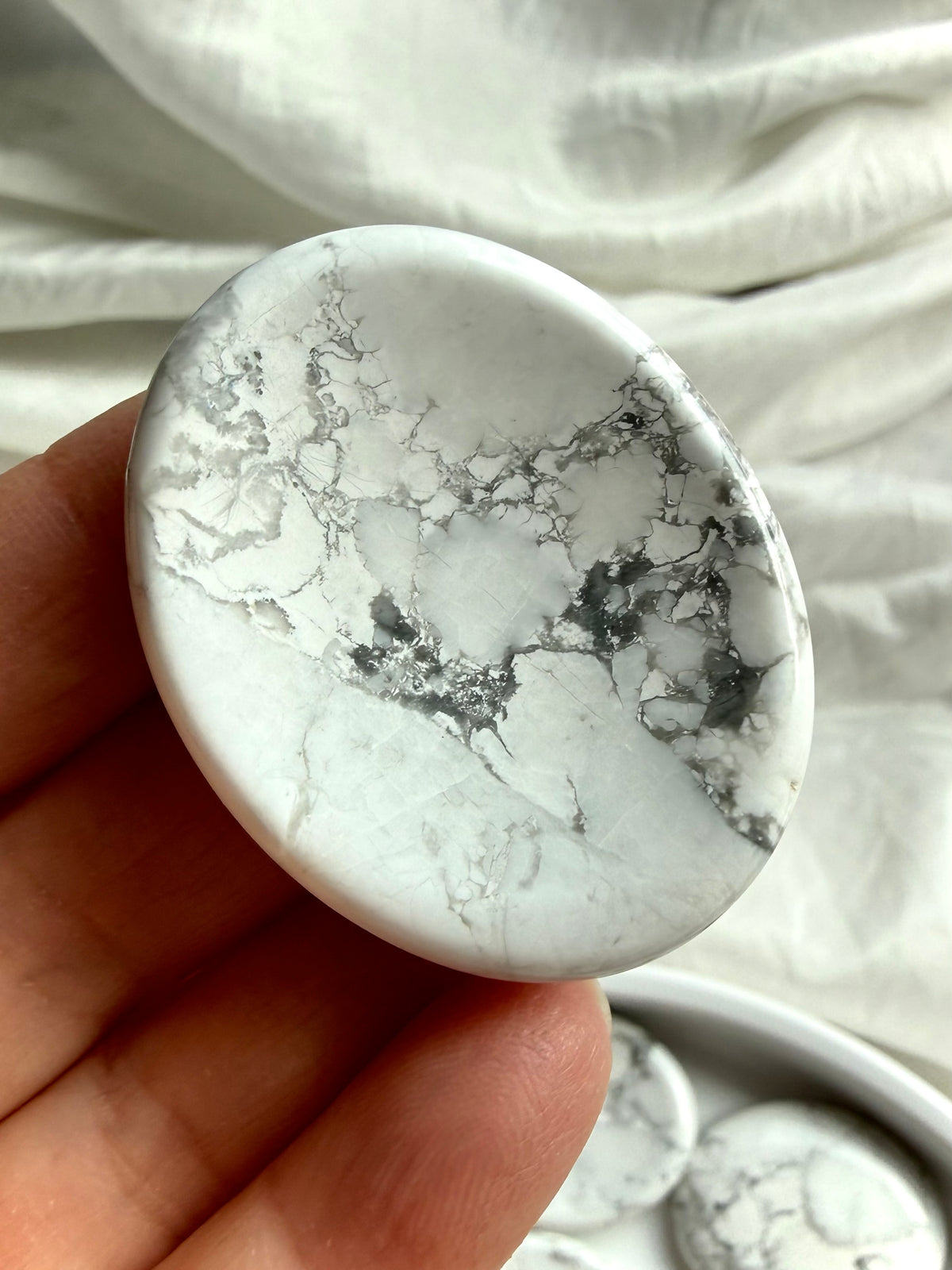White Howlite thumb stone held in hand with natural gray marbling for calm, meditation and mindful reflection