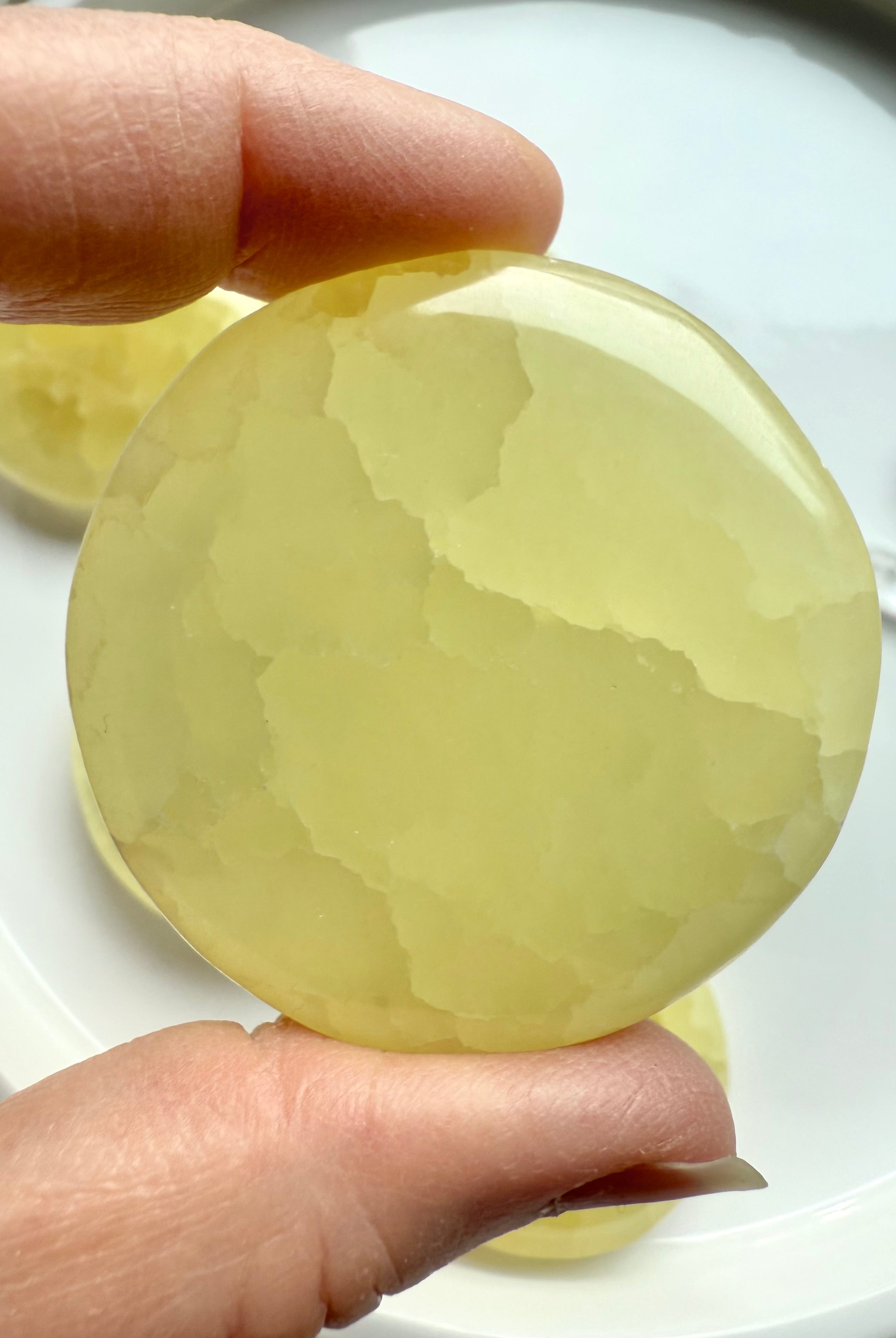 Lemon calcite disc held between fingers to show edge thickness and clarity