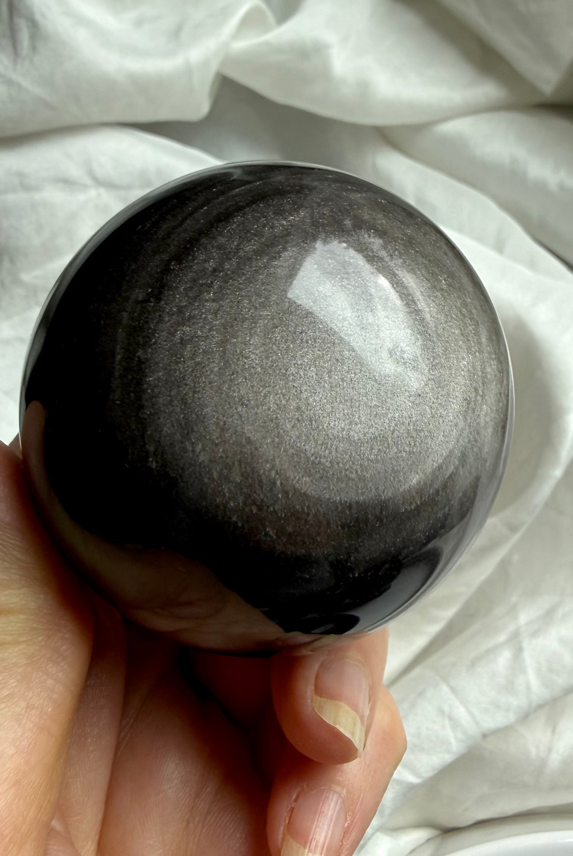 Detailed view of silver sheen pattern in polished Obsidian sphere, reflecting light and energetic movement