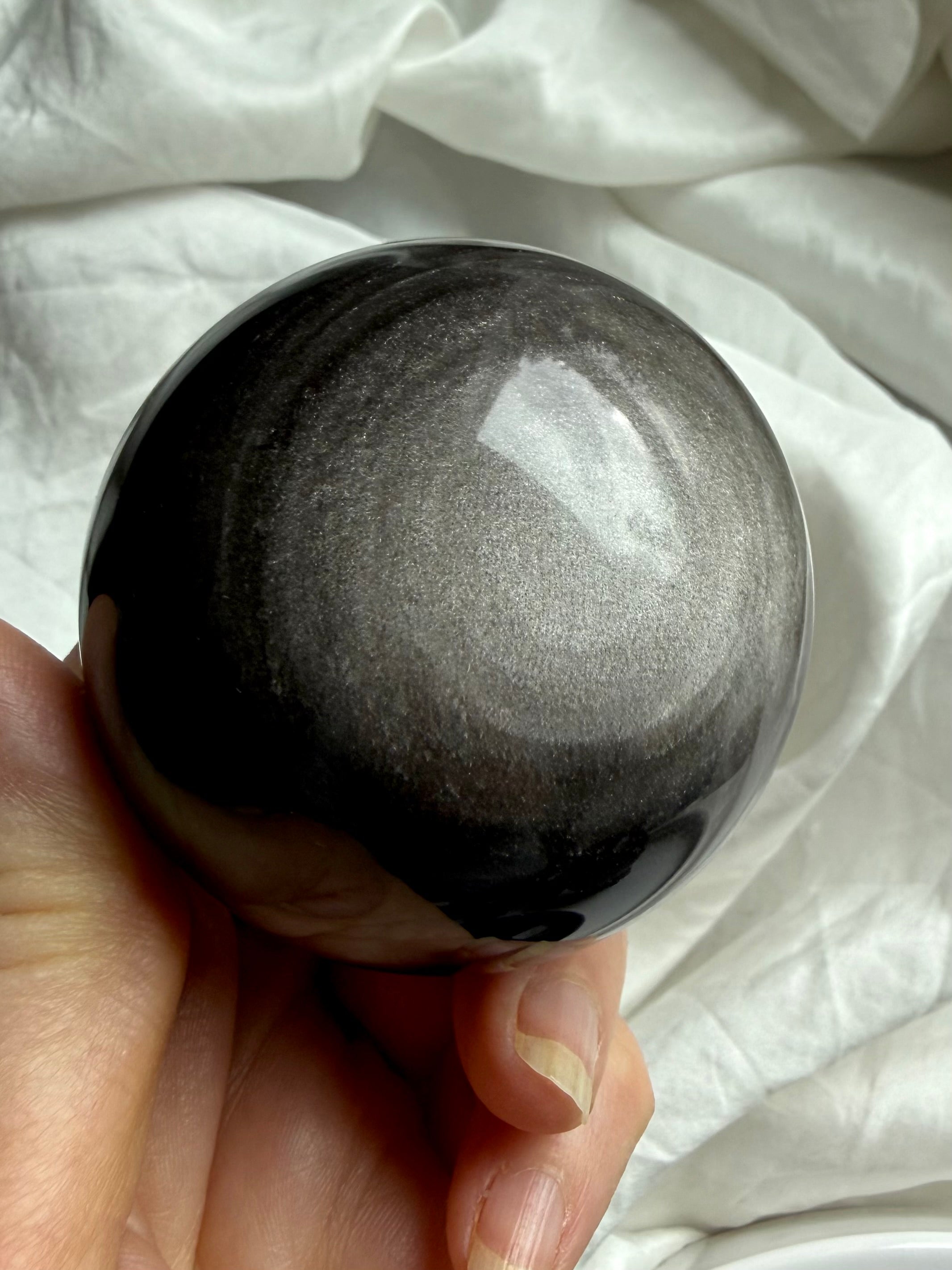 Detailed view of silver sheen pattern in polished Obsidian sphere, reflecting light and energetic movement