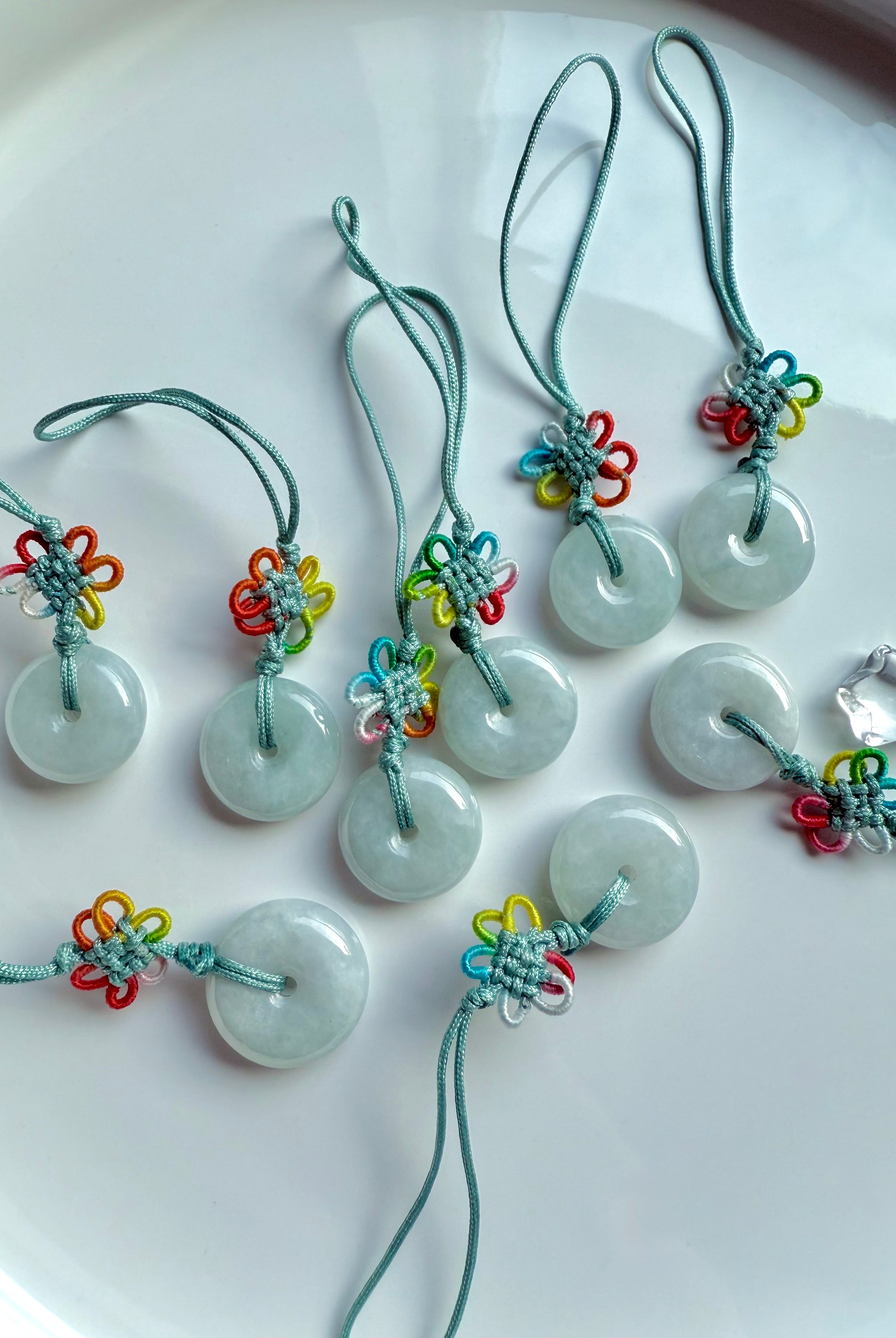 Group of natural jade donut charms with rainbow knot detail and green nylon cord shown on a white plate