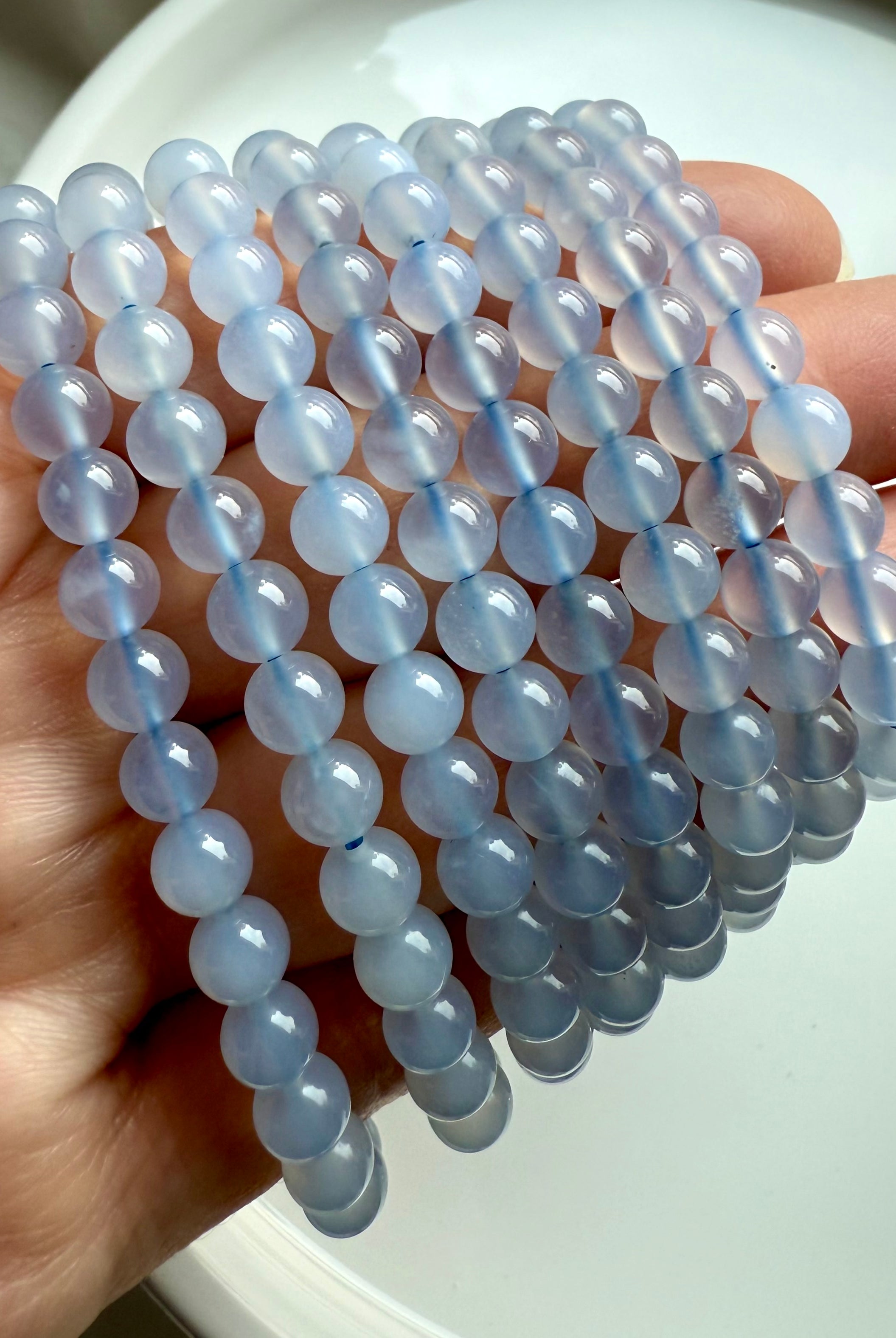 Layered Blue Chalcedony stretch bracelets fanned out in hand, showing polished round beads and dreamy blue tones
