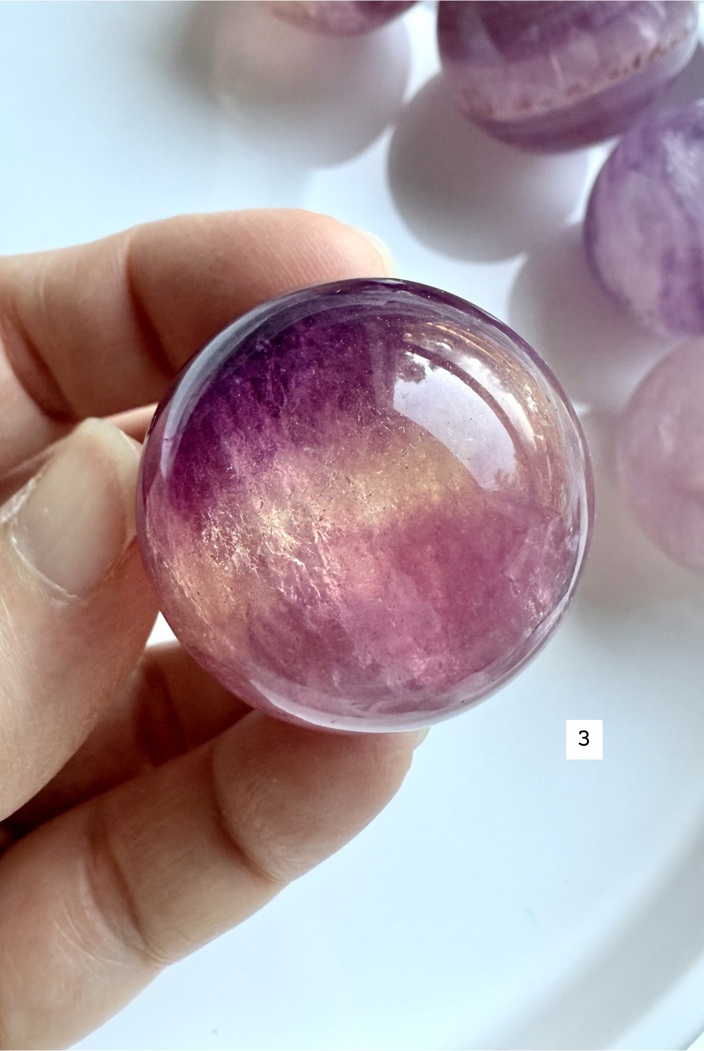 polished Candy Fluorite sphere with vibrant magenta and purple layers held in hand for intuitive energy