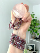 Green Unicorn Stone bracelets โ aka Watermelon Tourmaline in Lepidolite โ stacked on wrist and held with rose quartz sphere. Heart chakra jewelry for love, grief support + calm