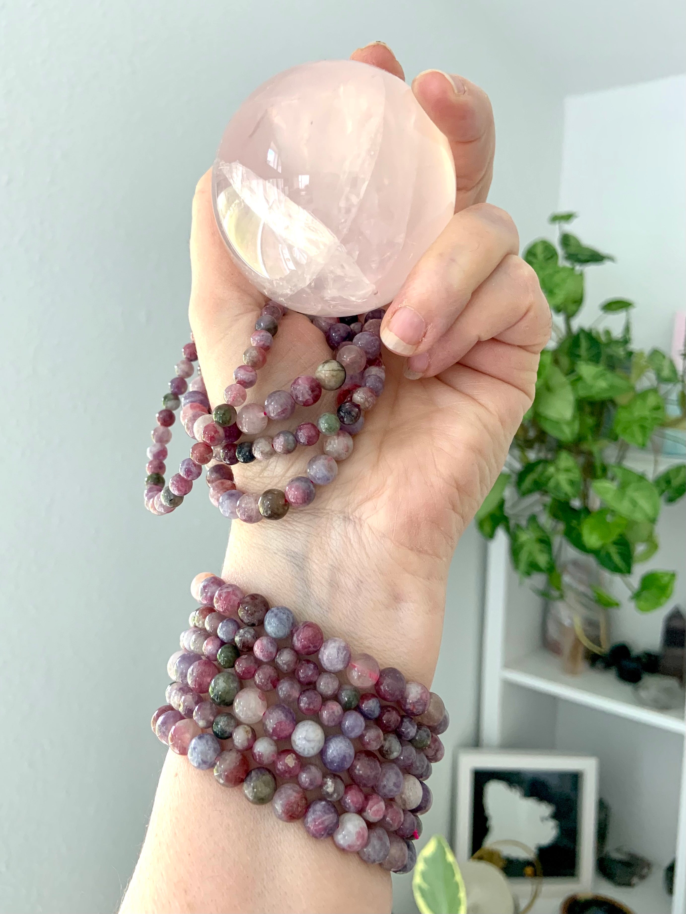 Green Unicorn Stone bracelets โ aka Watermelon Tourmaline in Lepidolite โ stacked on wrist and held with rose quartz sphere. Heart chakra jewelry for love, grief support + calm