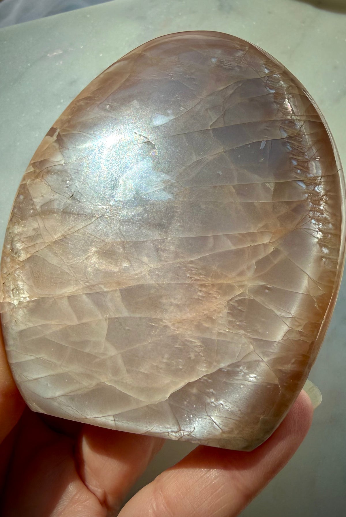 Peach Moonstone freeform held in hand with luminous silver flash, warm golden shimmer and natural rainbow iridescence