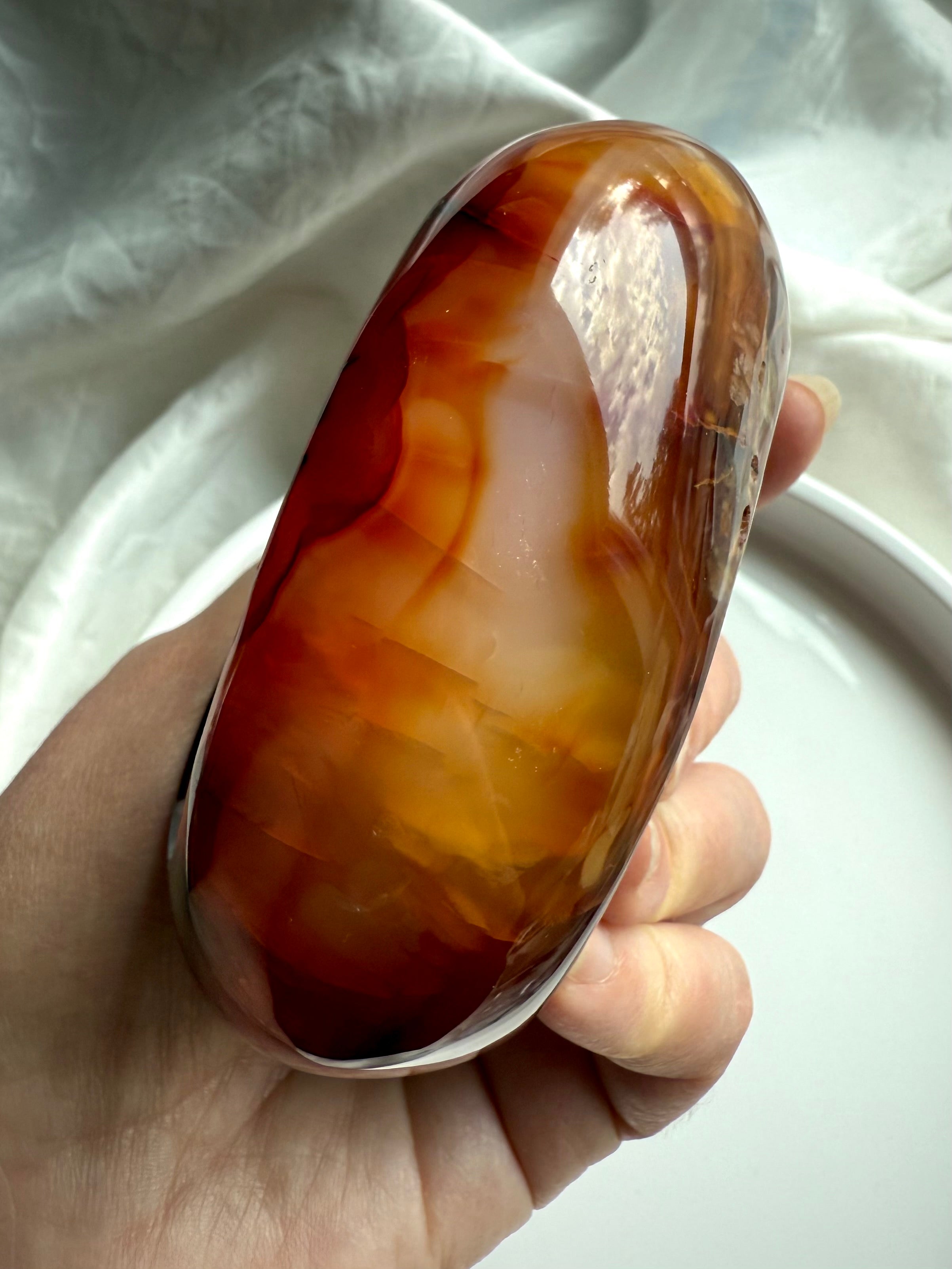 Side profile of Carnelian crystal bowl held in hand, highlighting translucent layers of orange and amber tones.