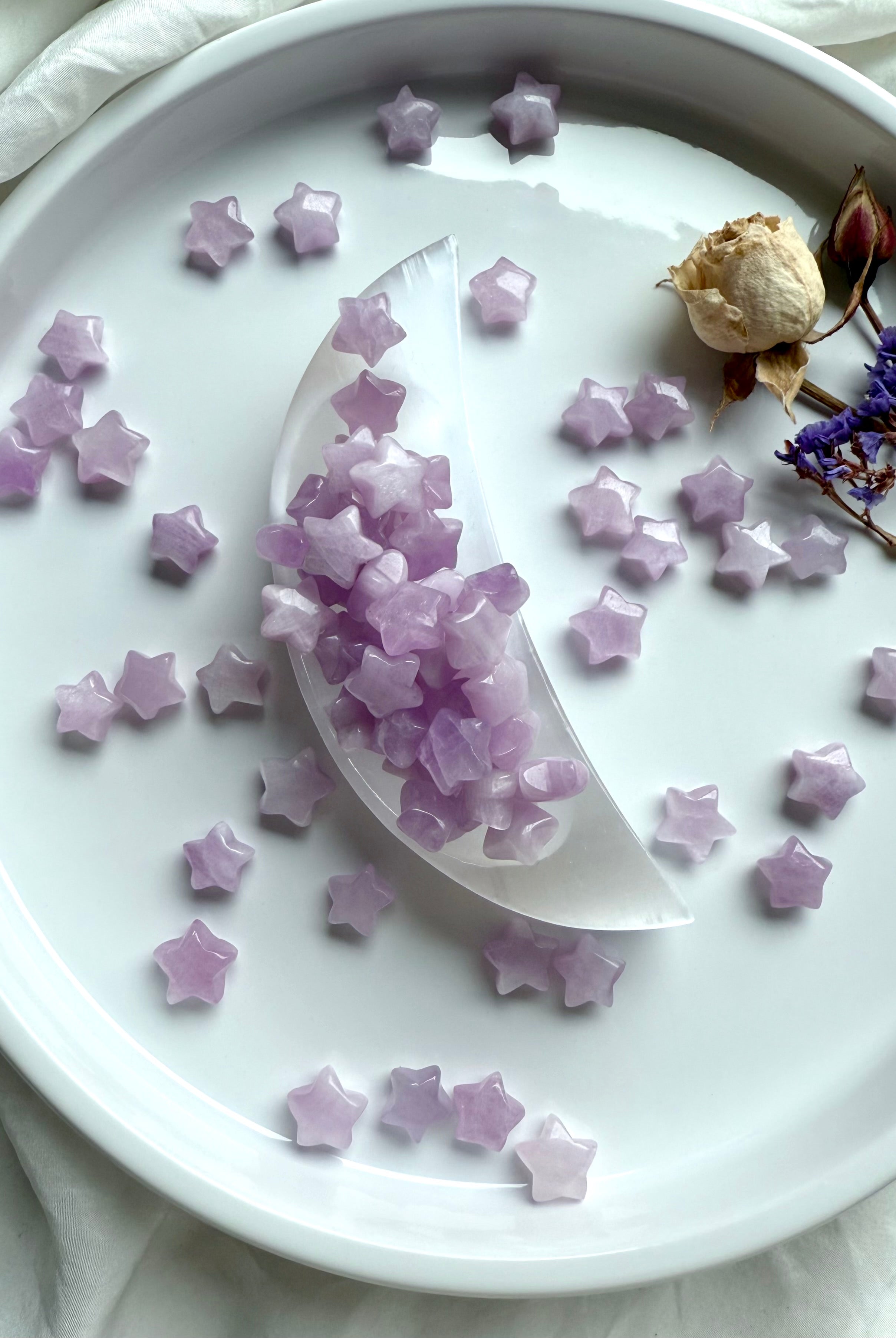 Kunzite mini stars spilling from a selenite moon dish, surrounded by dried flowers on white plate — celestial altar crystal styling.