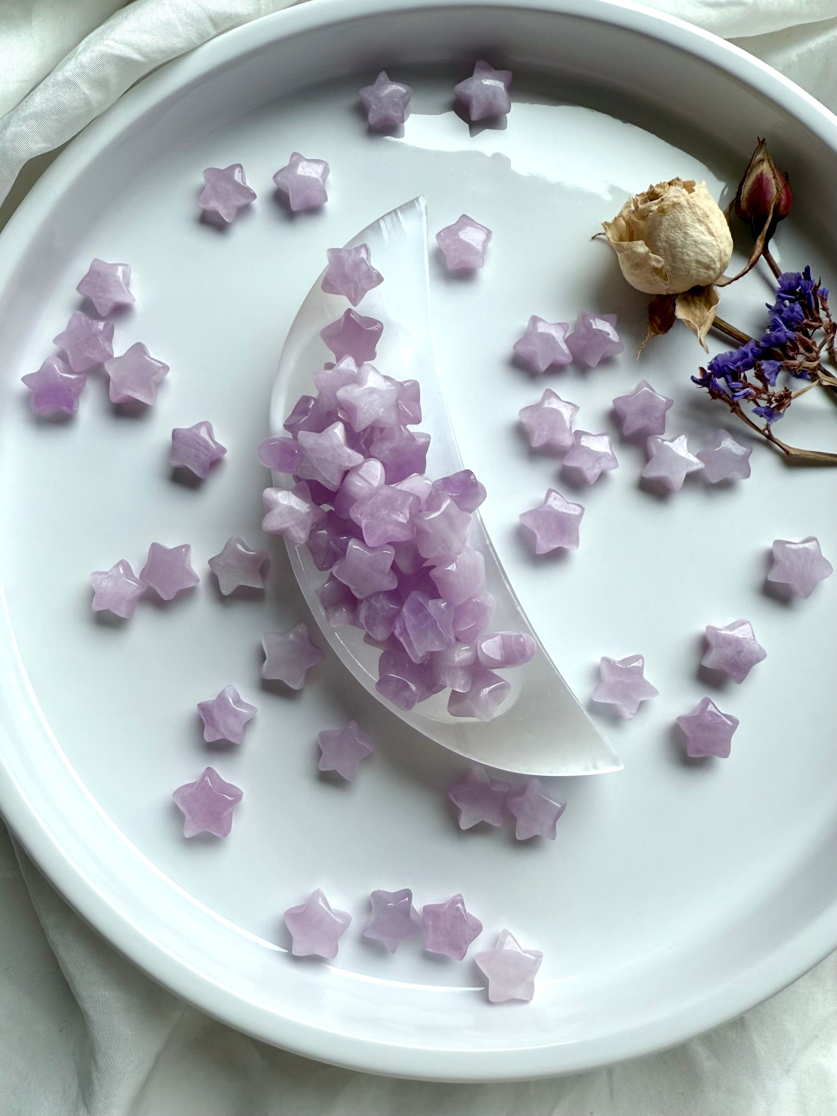 Kunzite mini stars spilling from a selenite moon dish, surrounded by dried flowers on white plate — celestial altar crystal styling.