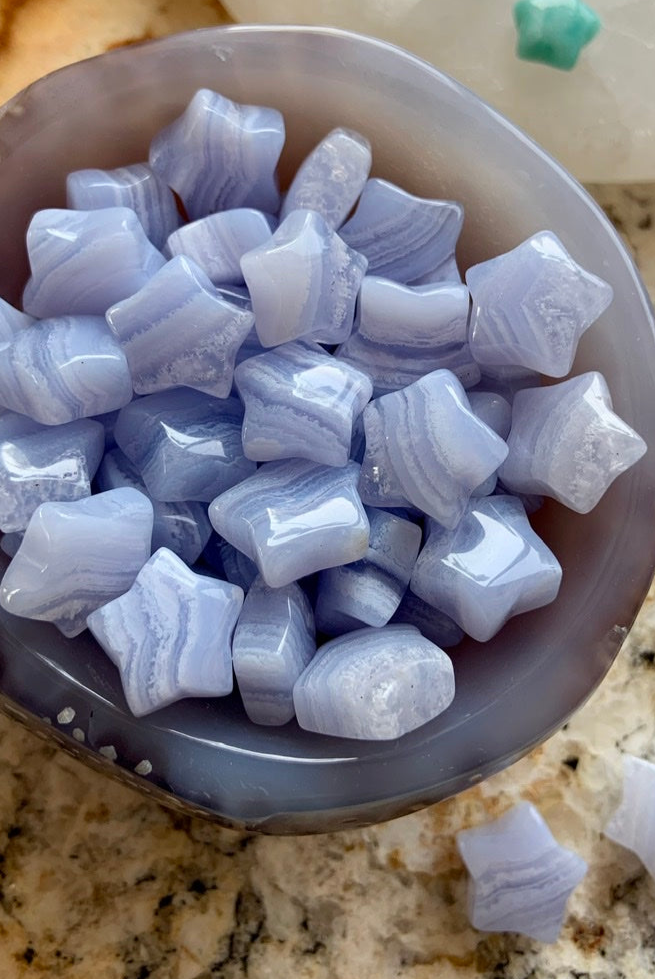Close-up of blue/gray agate bowl filled with Mini Blue Lace Agate stars — soothing crystals for gentle communication & emotional peace.