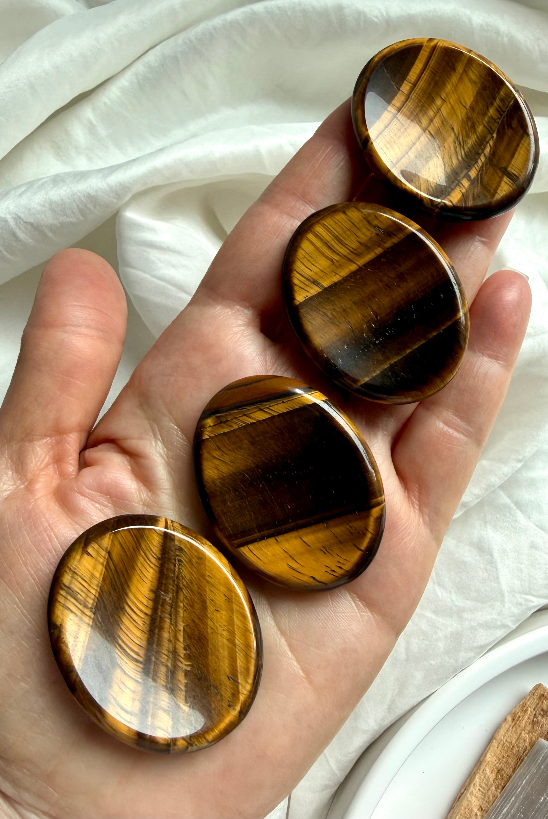 hand holding tiger’s eye worry stone showing silky golden brown banding, crystal for confidence courage and grounding energy