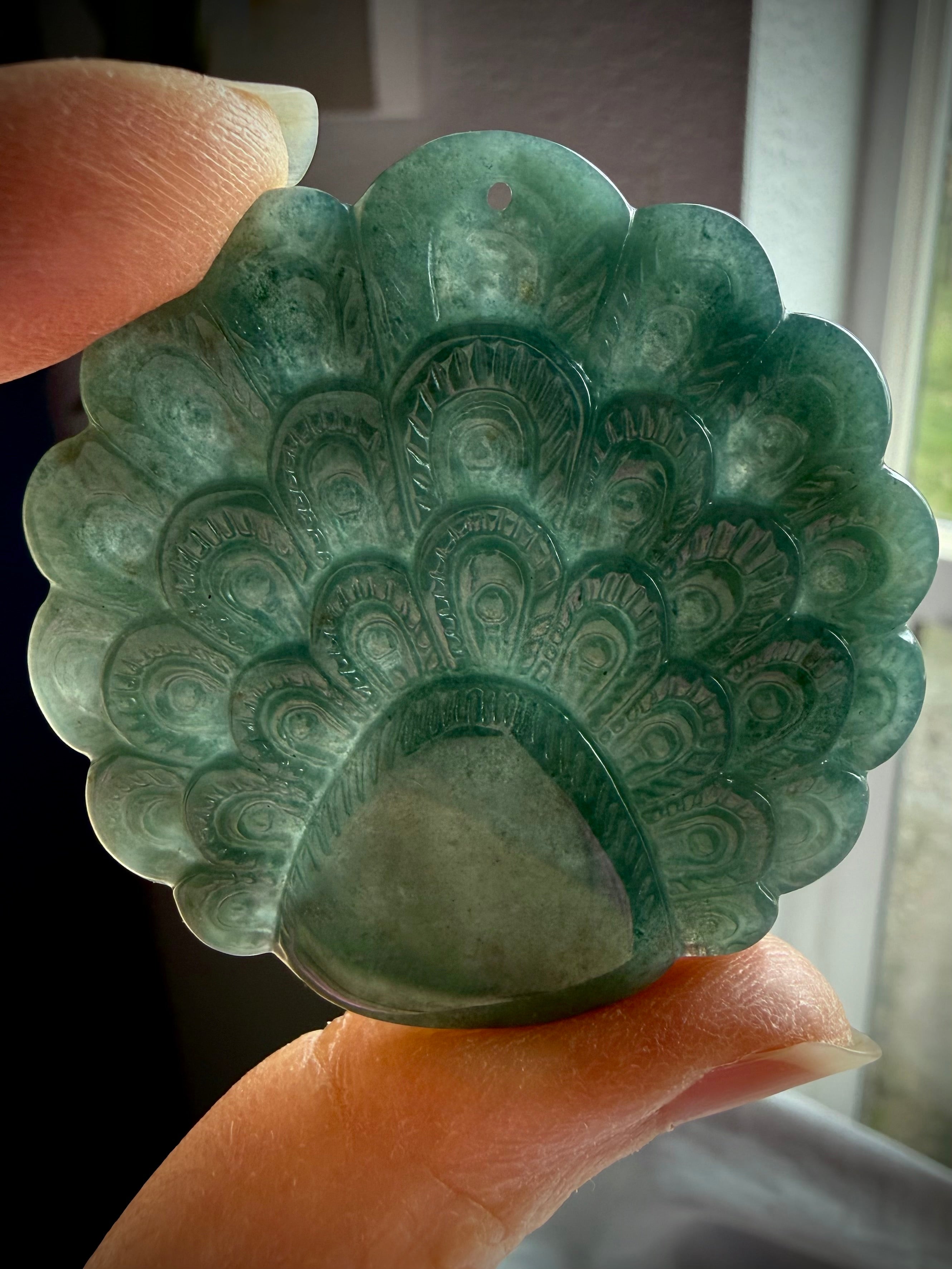 Reverse side of a translucent Blue Water Jade peacock medallion displaying intricate feather details
