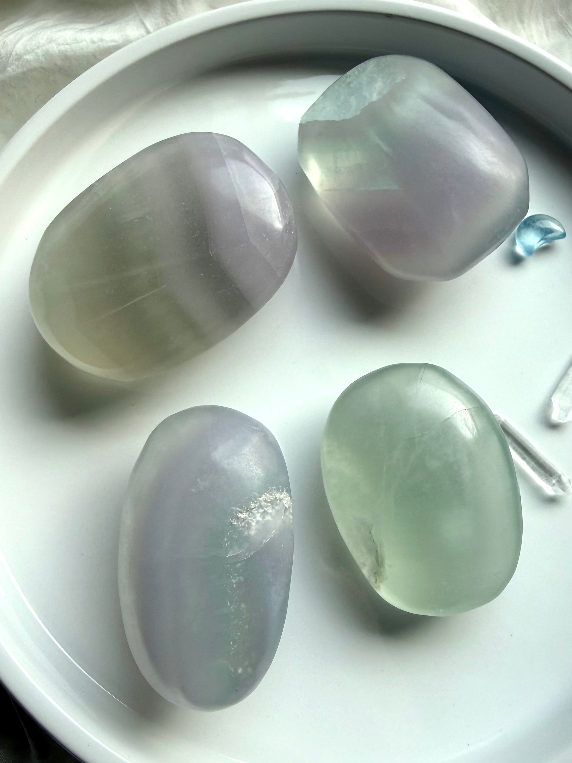 yttrium fluorite palm stones in soft pastel green and lavender tones on a white dish showing full assortment with natural banding and translucency