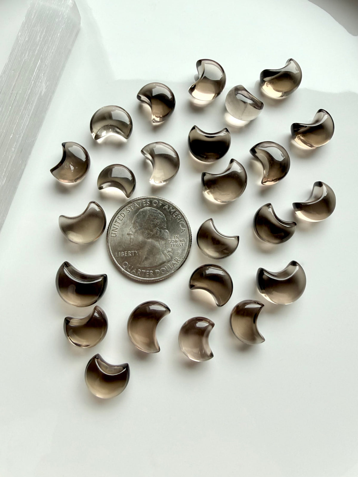 Smoky Quartz moon carvings next to a US quarter for scale, tiny crescent shapes with smoky brown tones and beautiful translucence