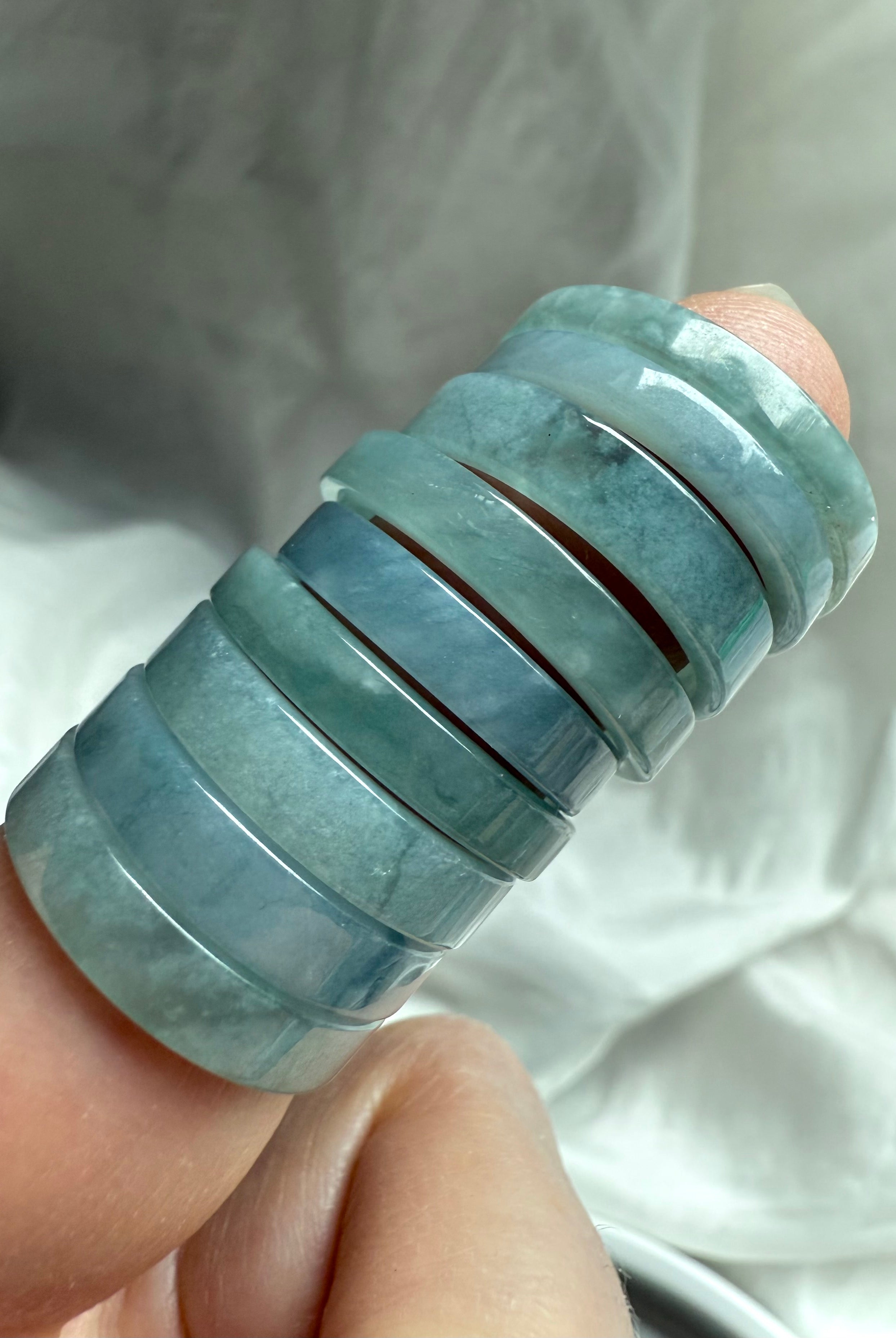 Close-up of flat Blue Water Jade rings stacked on finger, showing natural variation in tone