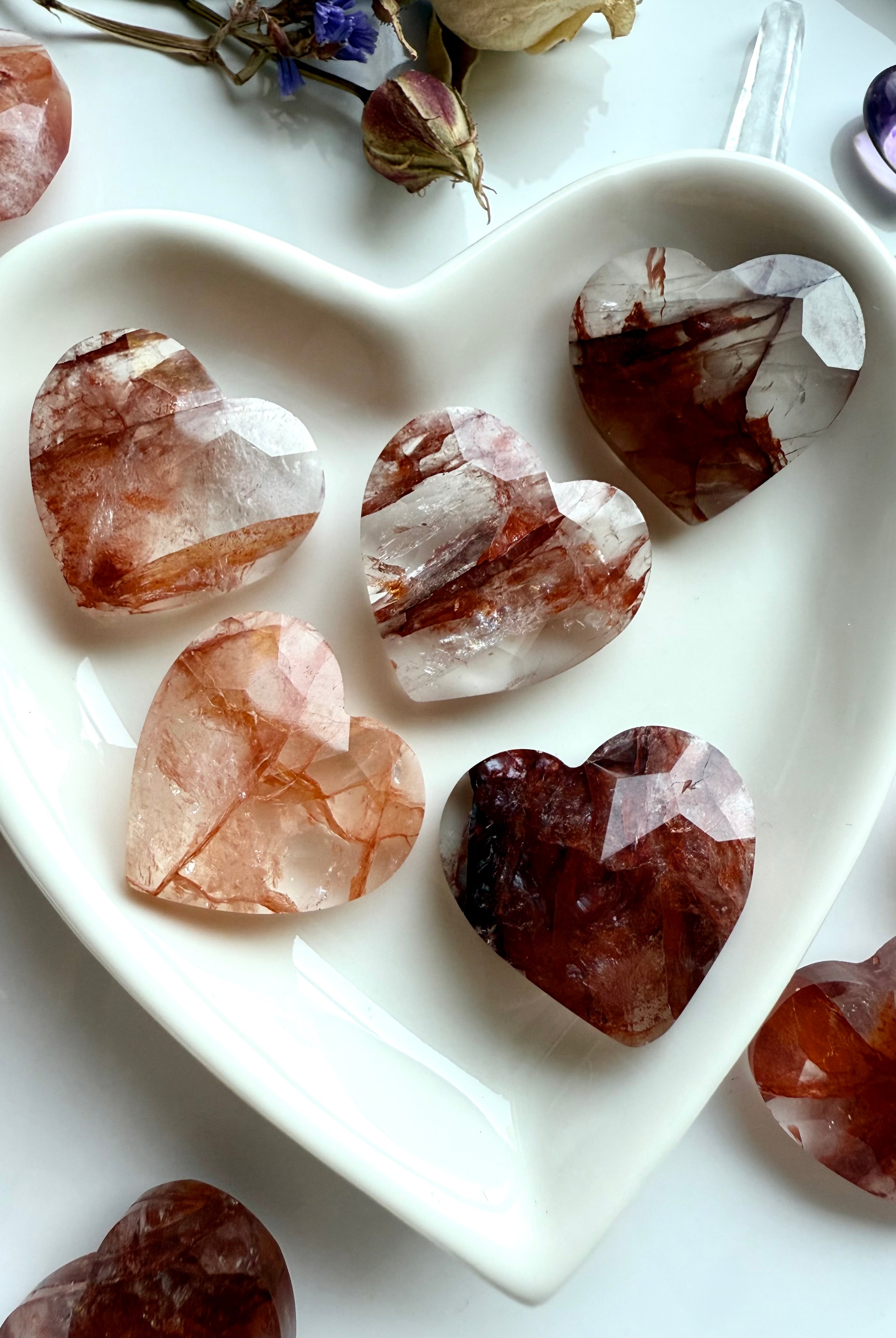 Close-up of faceted Fire Quartz hearts in a white heart bowl – polished hematoid quartz carvings for Root Chakra healing and energy clearing