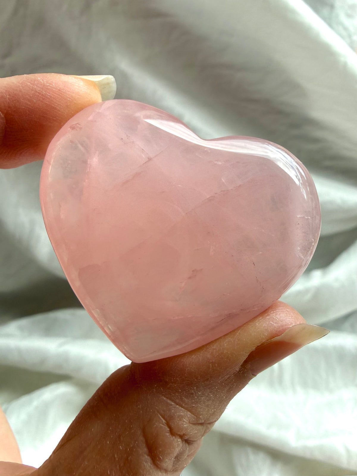 Large polished Rose Quartz heart held in hand with luminous pink color and subtle natural variations