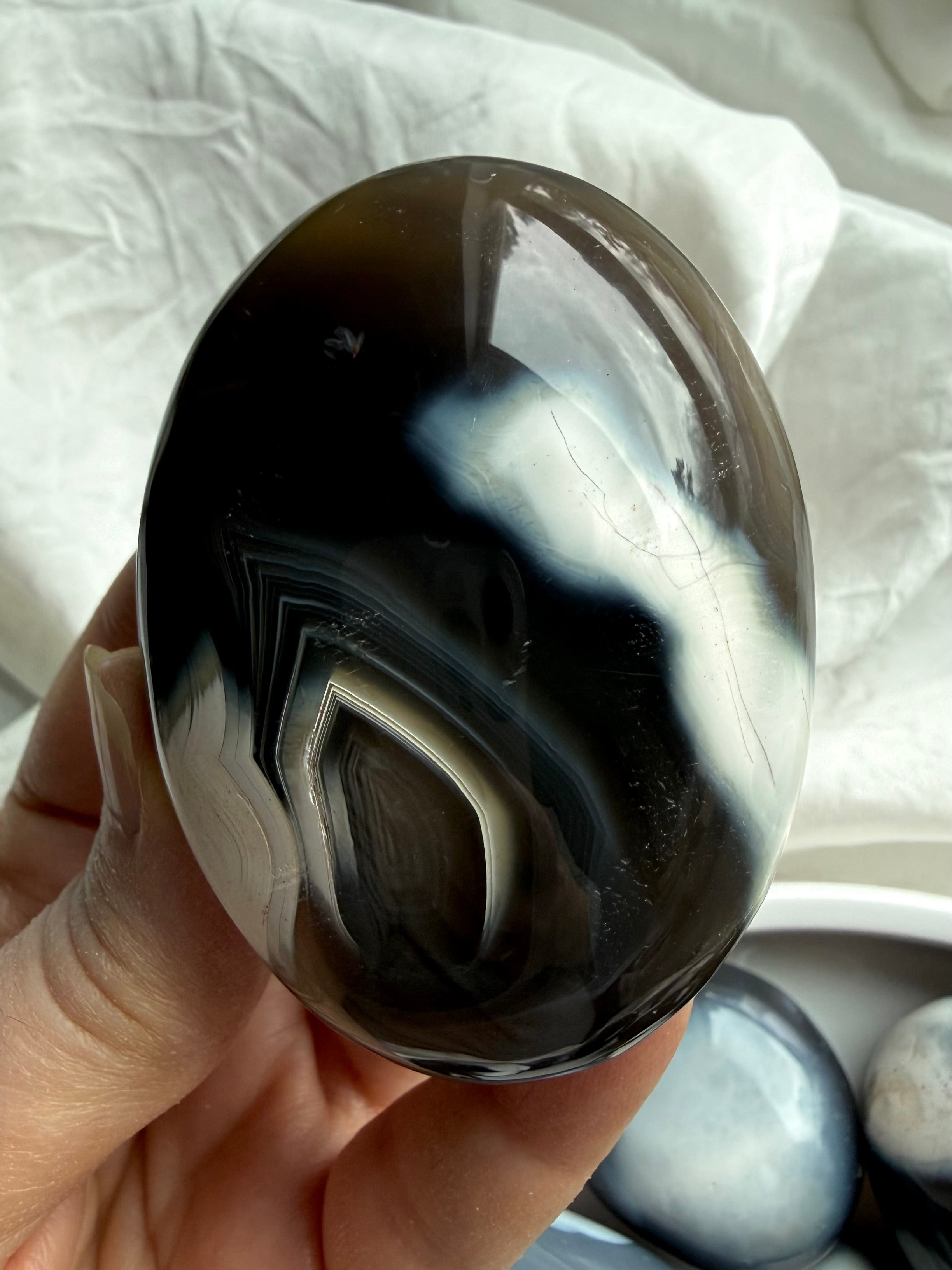 Orca Agate palm stone held in hand, highlighting smooth polish and layered black and white agate patterns for grounding energy