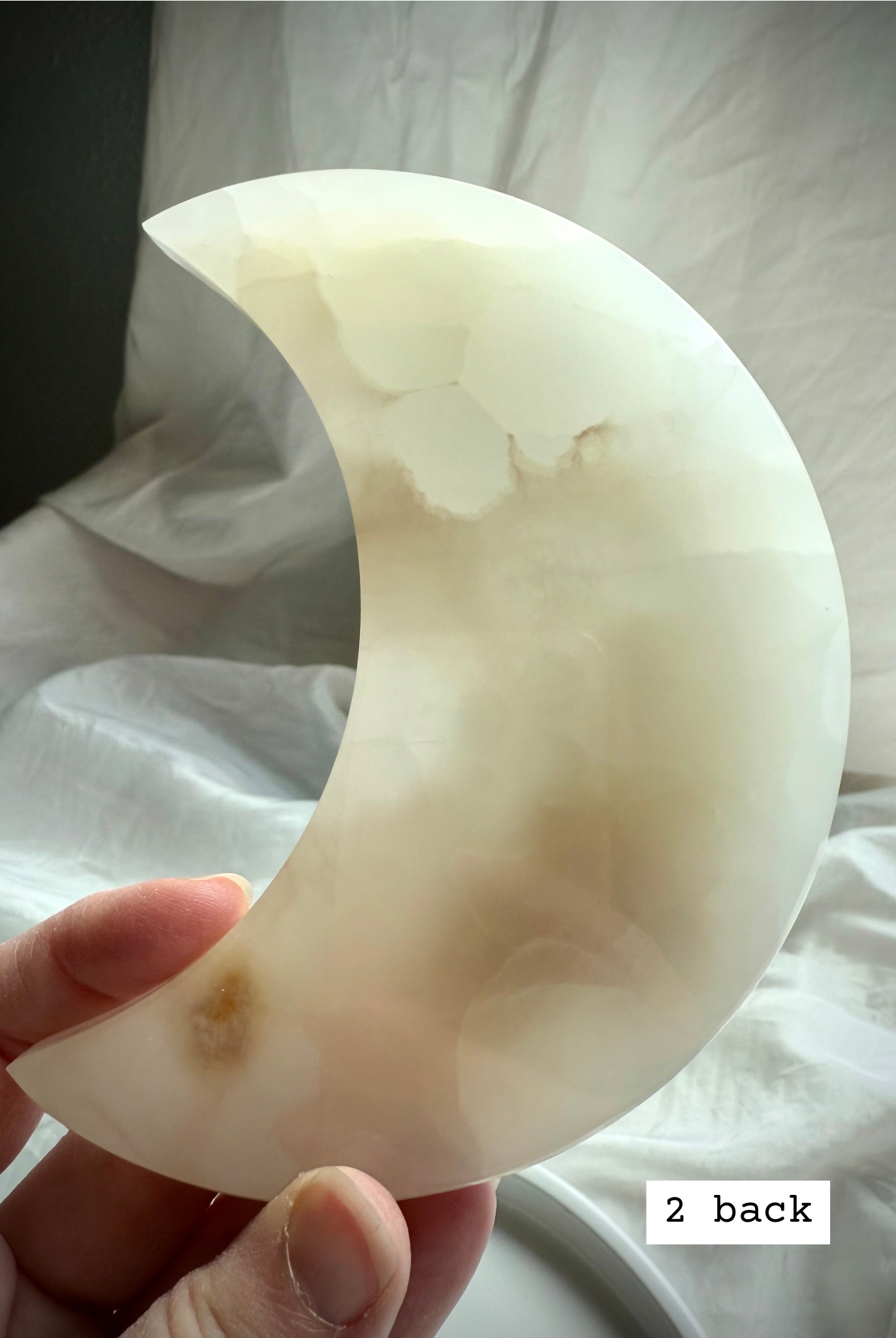 White Onyx Crescent Moon Plate held to the light showing pale creamy white and golden hues, back view.