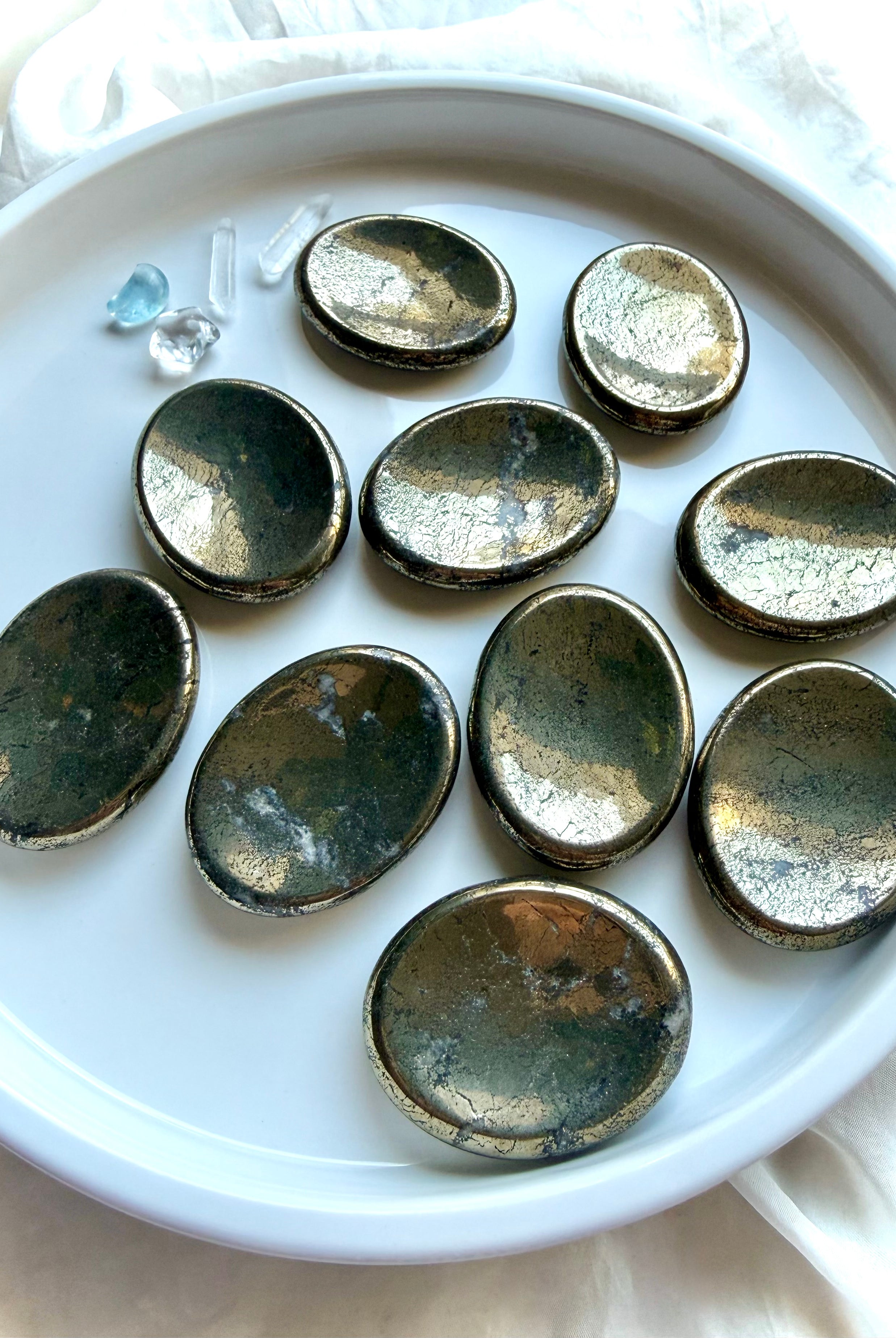 Pyrite worry stones arranged on a white dish with brilliant metallic luster and natural mineral variation