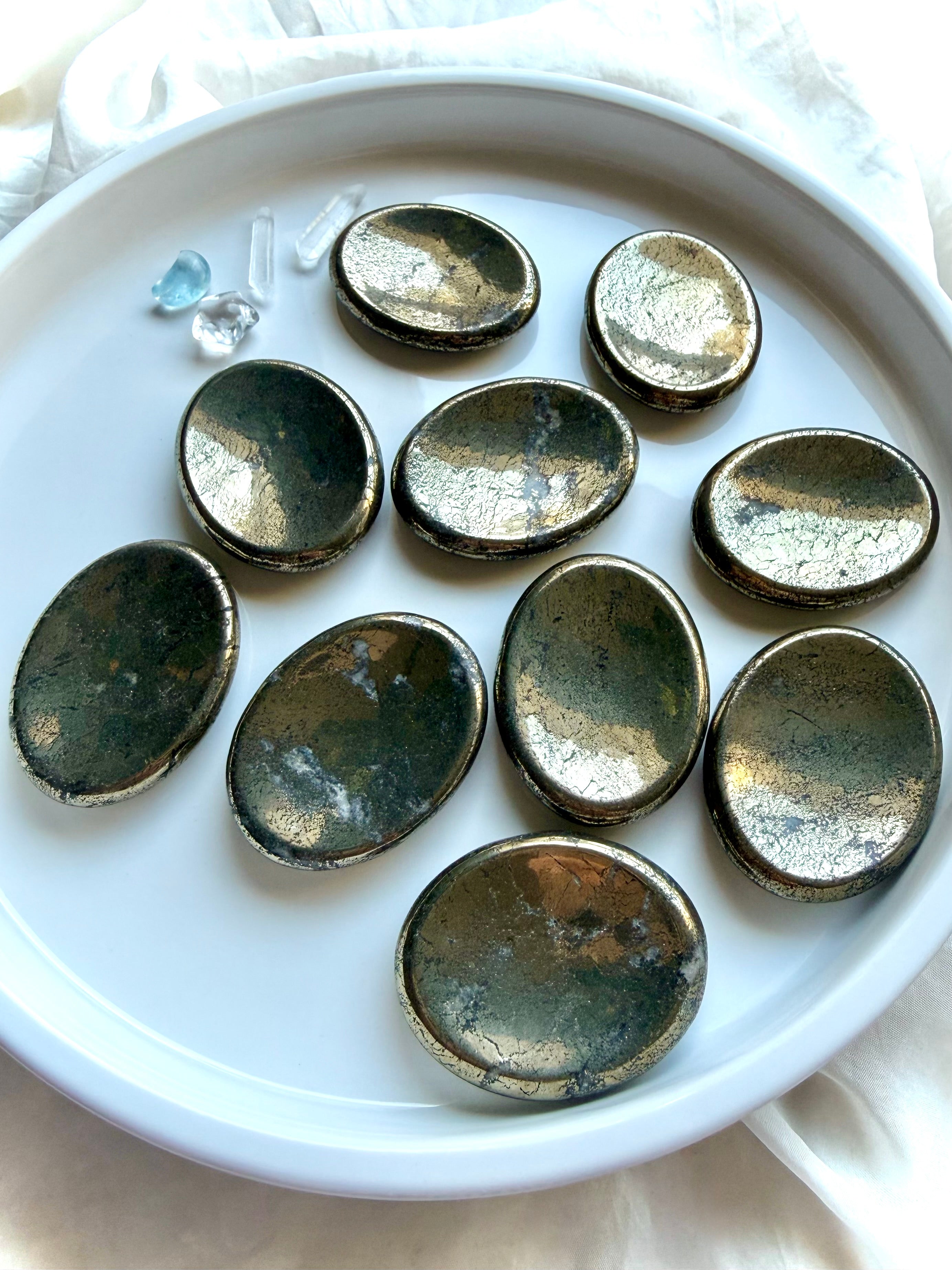 Pyrite worry stones arranged on a white dish with brilliant metallic luster and natural mineral variation