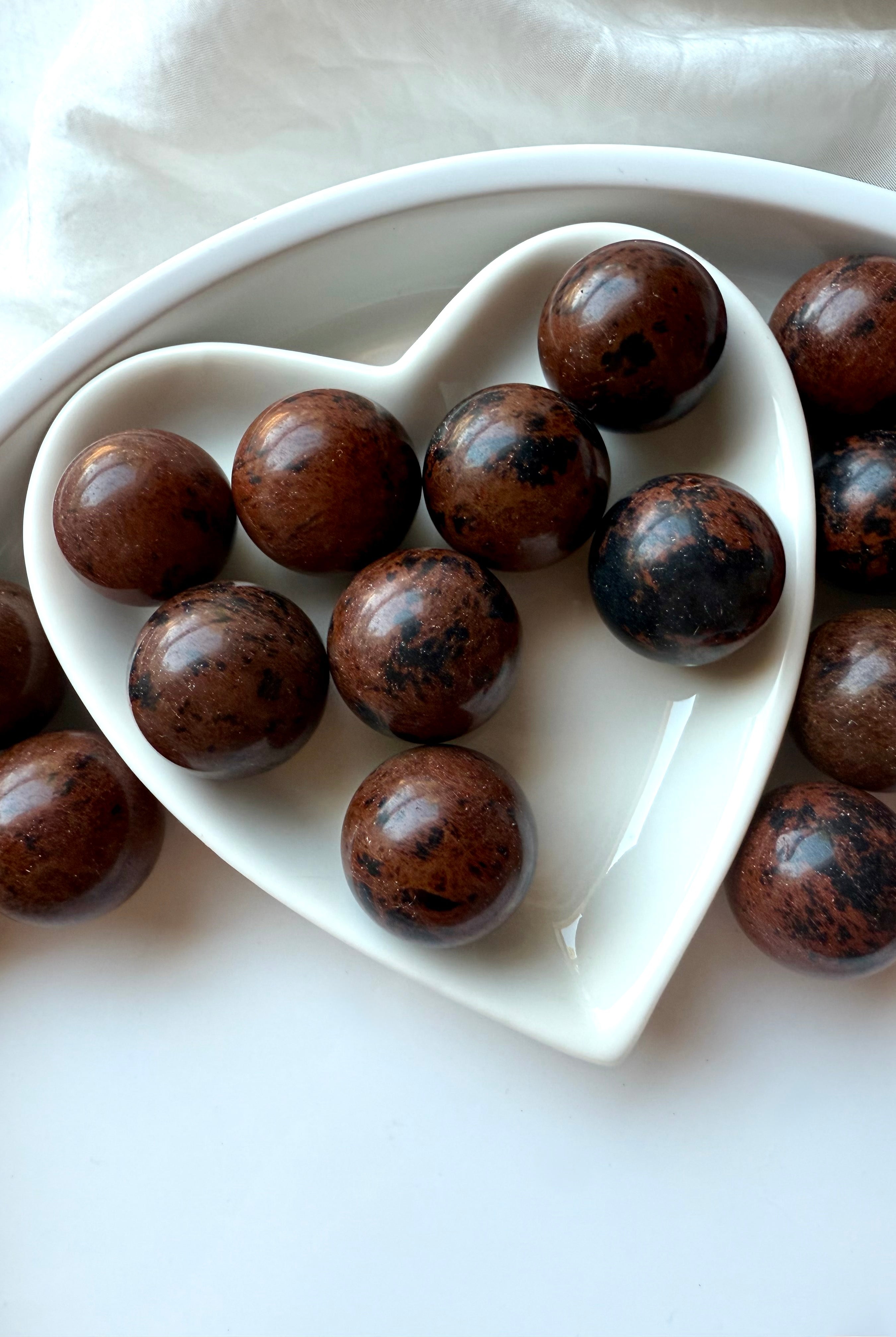 Polished Mahogany Obsidian crystal spheres displayed in white heart bowl – Root Chakra grounding stones