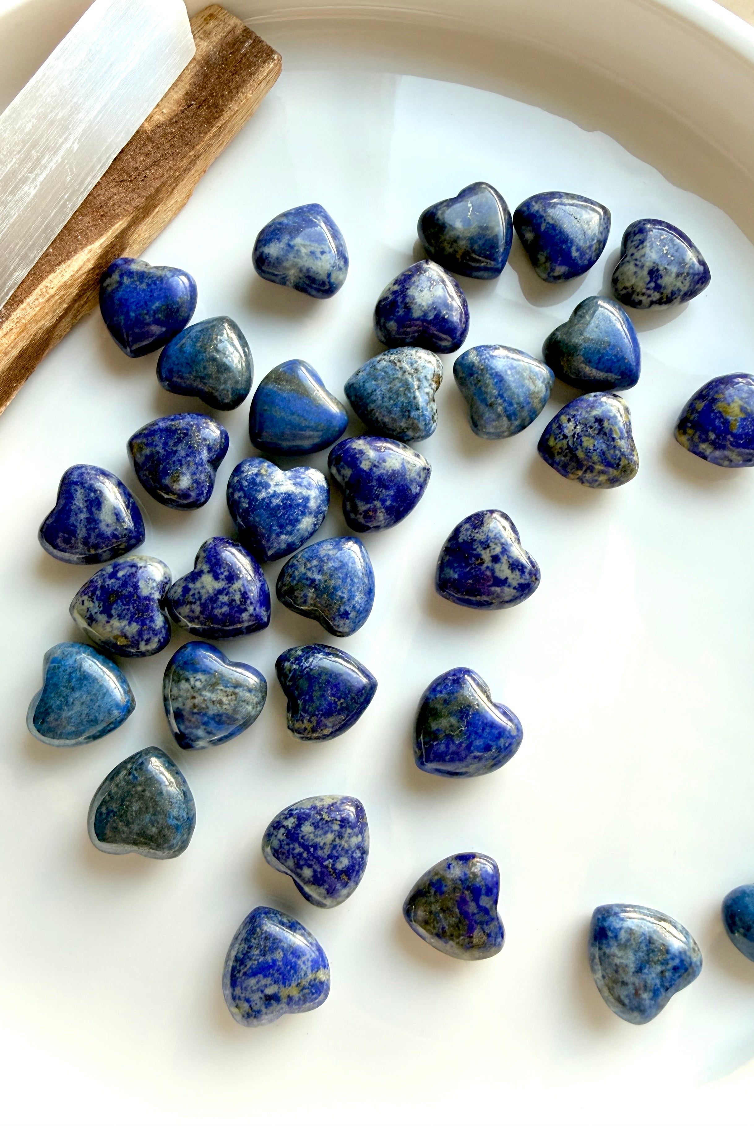 Mini Lapis Lazuli hearts arranged on a white tray, showcasing natural color variation and polished heart shapes, throat chakra healing crystals