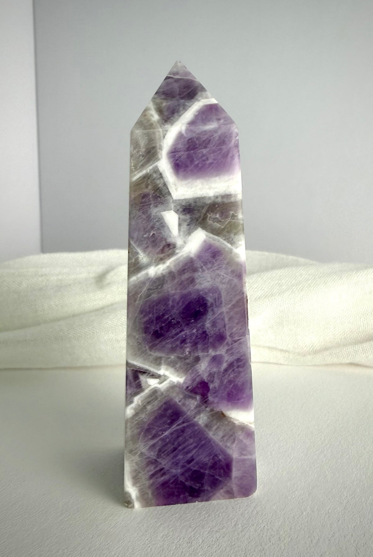 Chevron Amethyst tower standing upright, featuring rich violet crystal formations, white quartz bands and a polished pointed termination