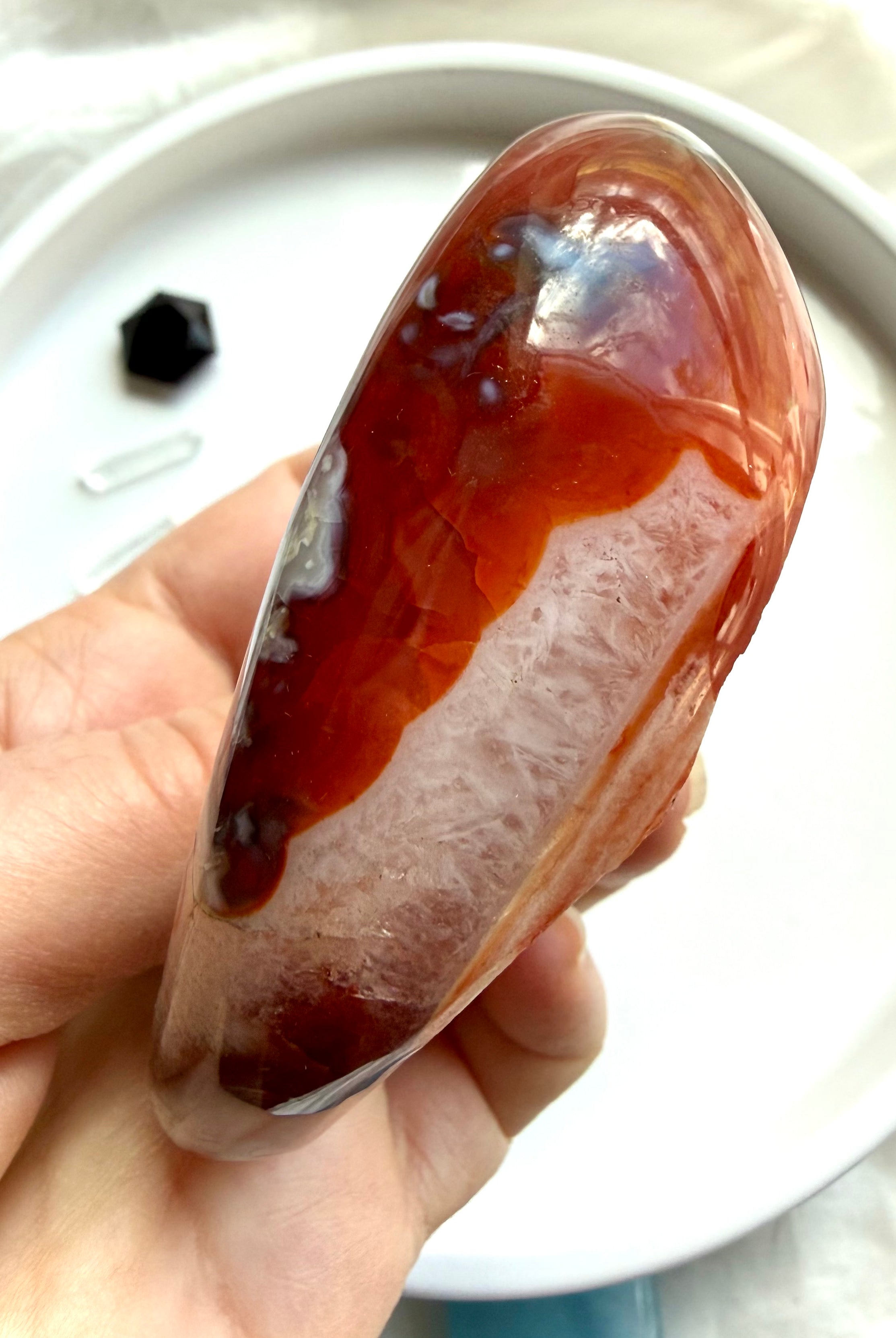 side view of polished carnelian stone bowl with quartz pattern and banded agate detail in hand