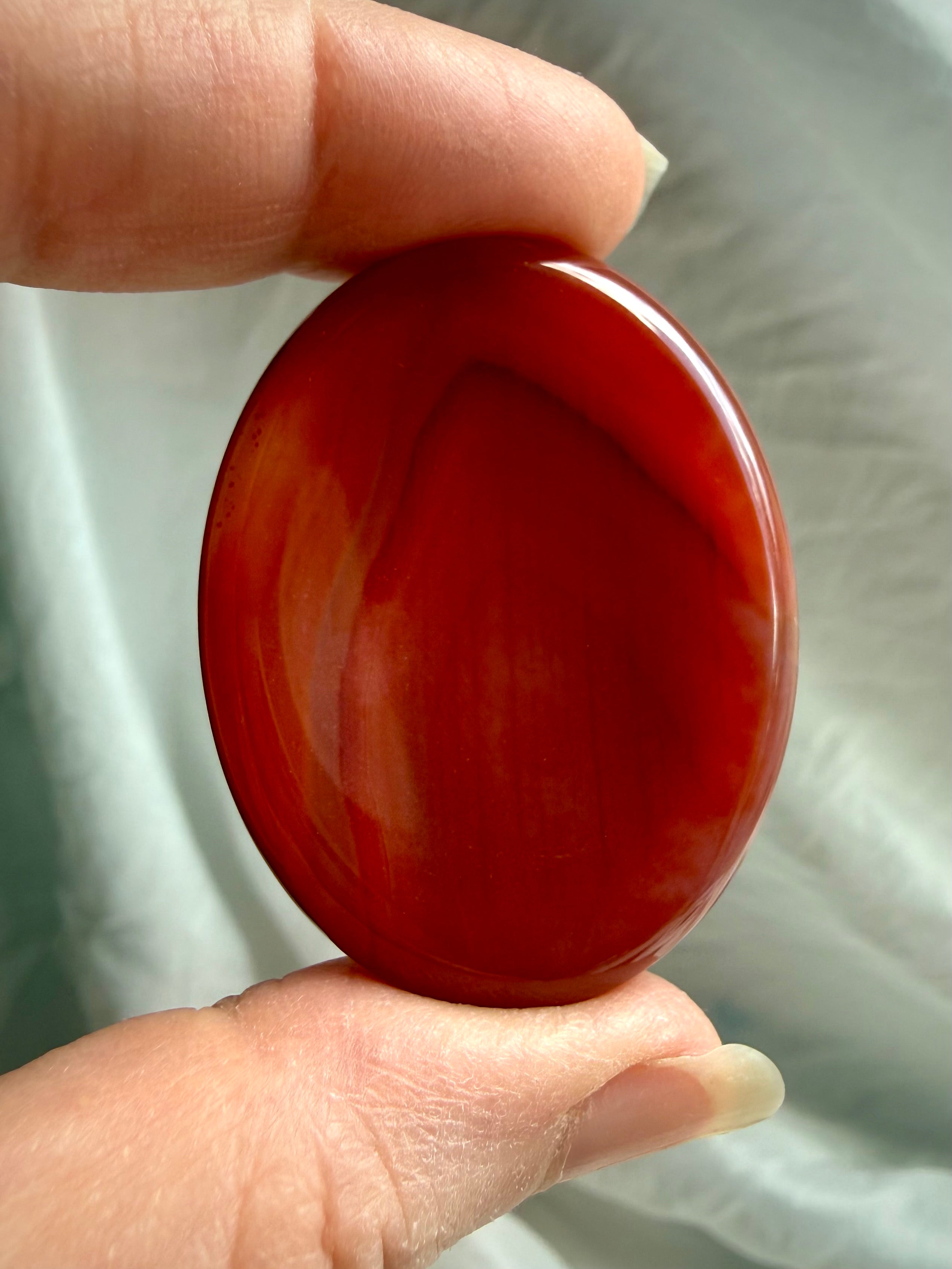 Deep red Carnelian worry stone held in hand, polished oval thumb stone for confidence, meditation and motivation