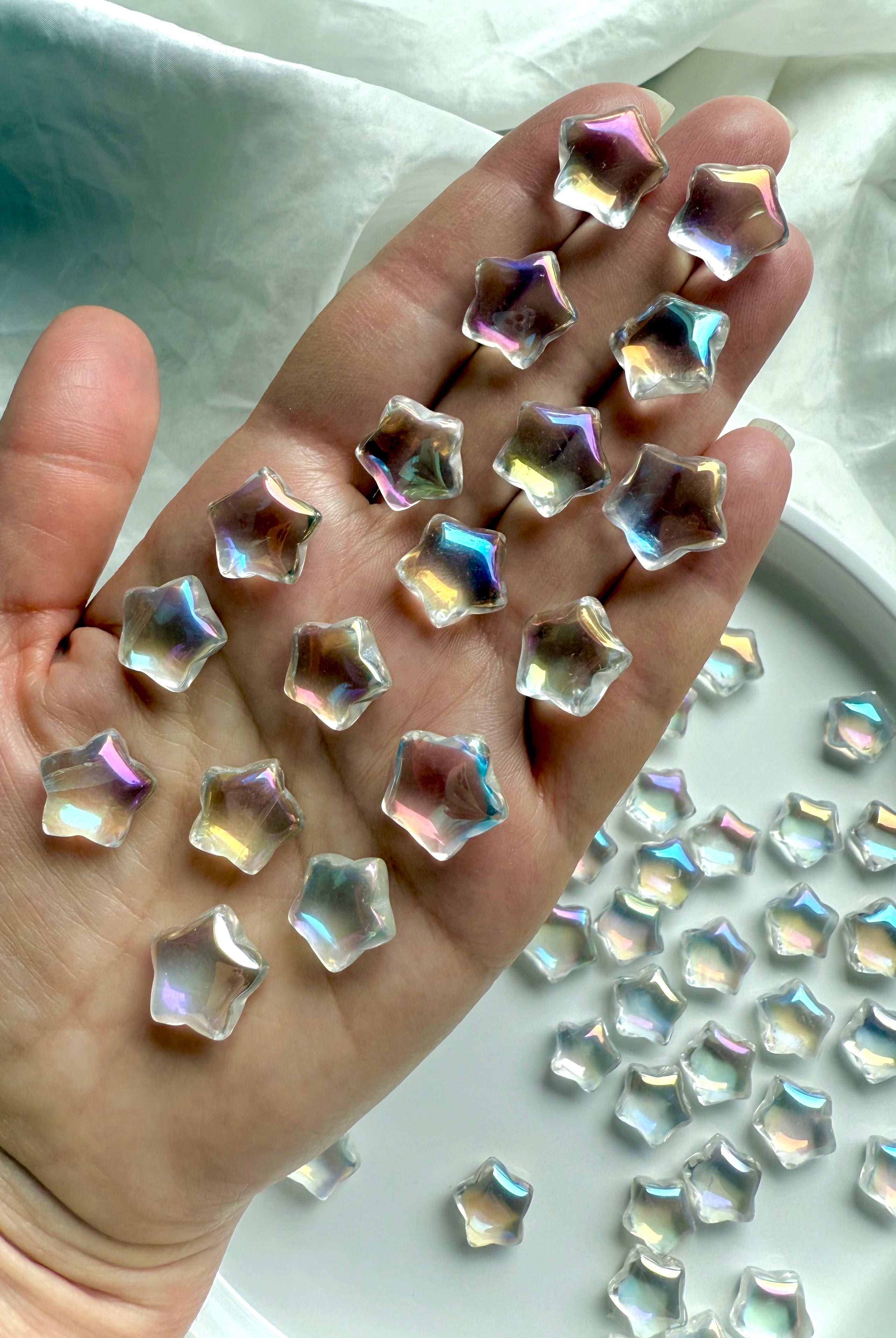 Hand holding mini aura quartz star carvings with opalescent rainbow light — pocket-sized crystals for healing, peace, and meditation