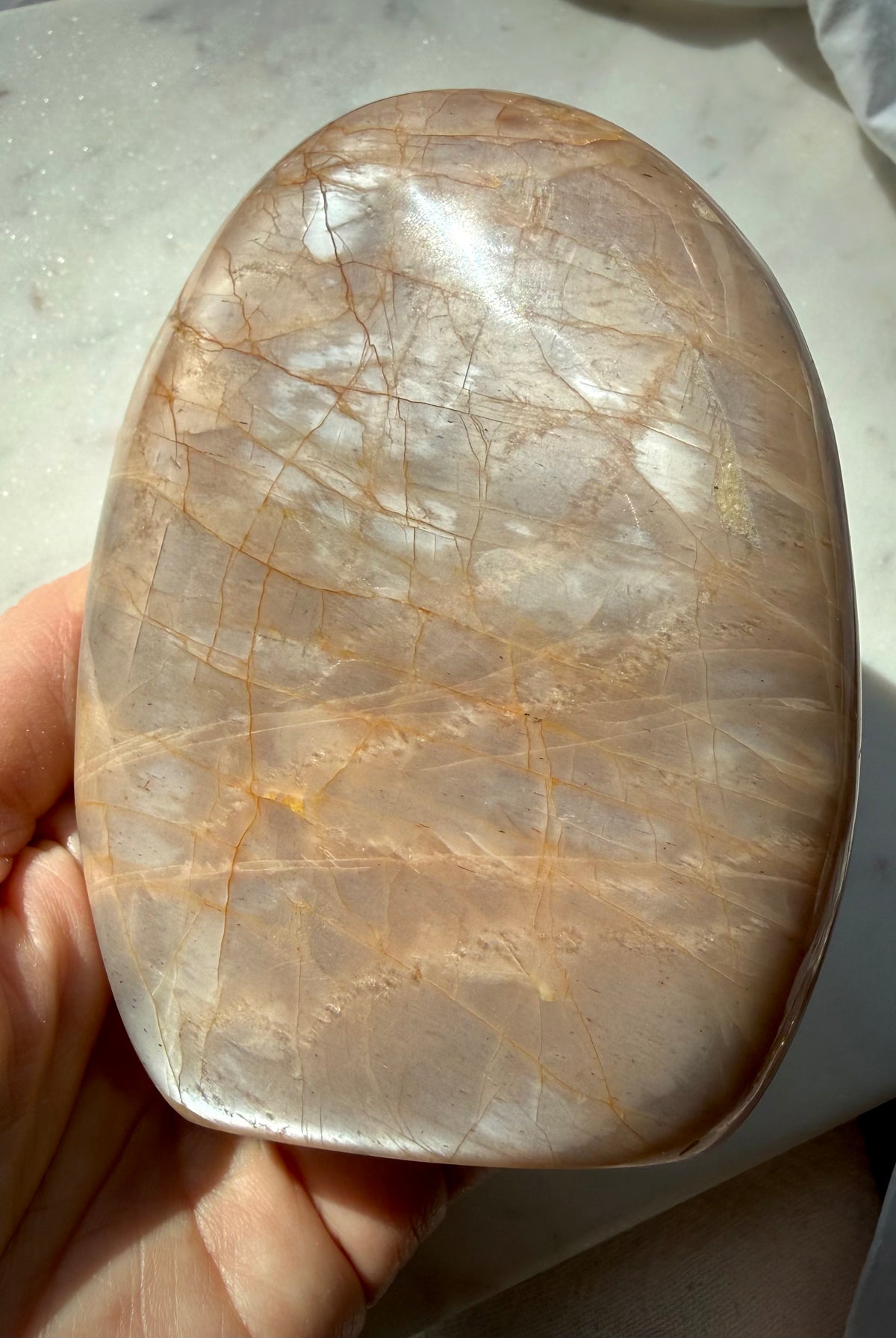 Polished Peach Moonstone crystal held in hand with luminous silvery sheen and natural peach color variations