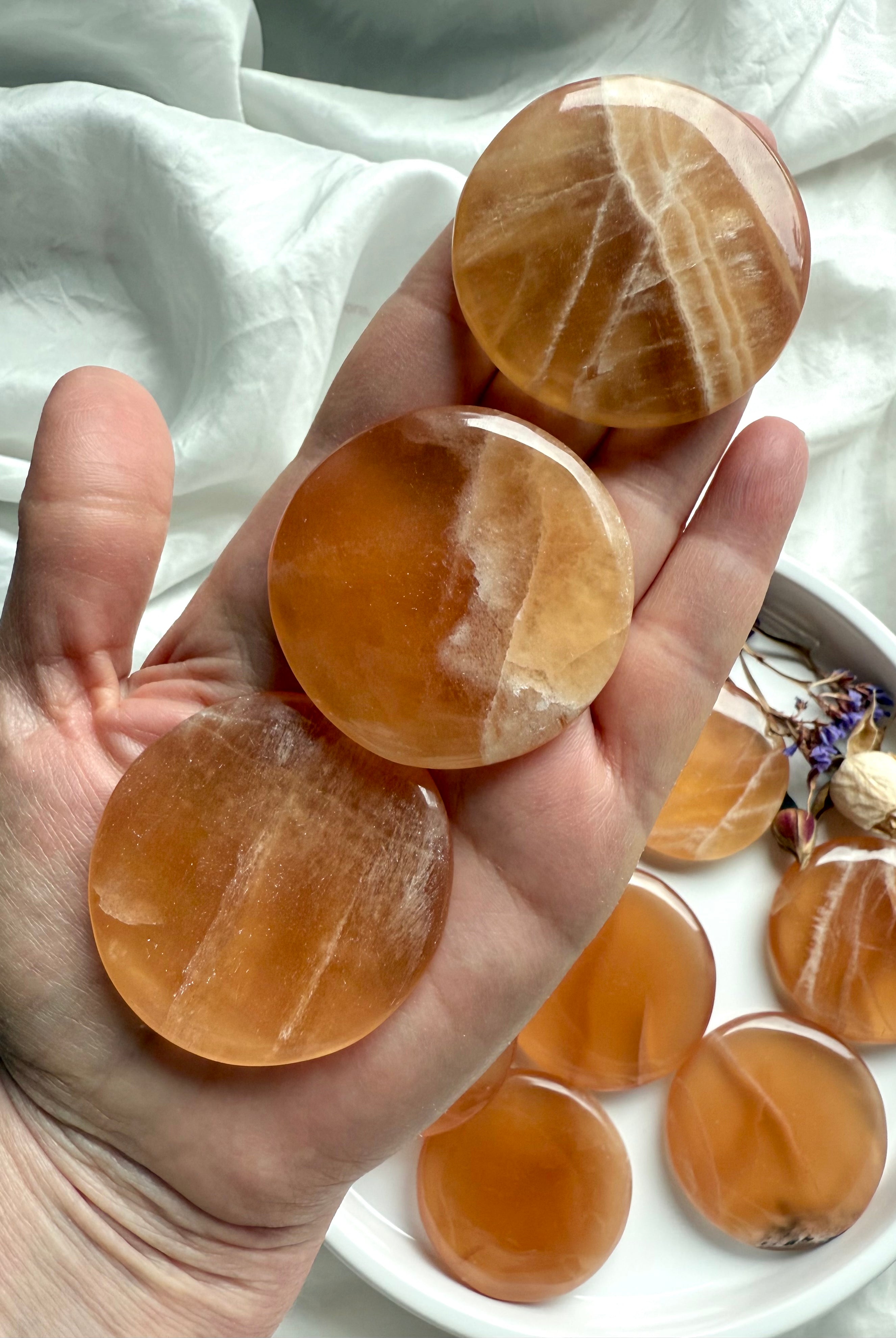 Hand holding three polished honey calcite discs with natural banding and warm golden tones for confidence, clarity, and gentle empowerment.
